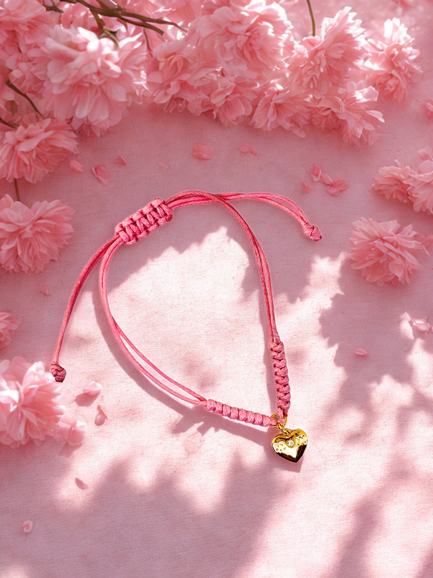 Pink braided bracelet with a heart charm on a pink floral background