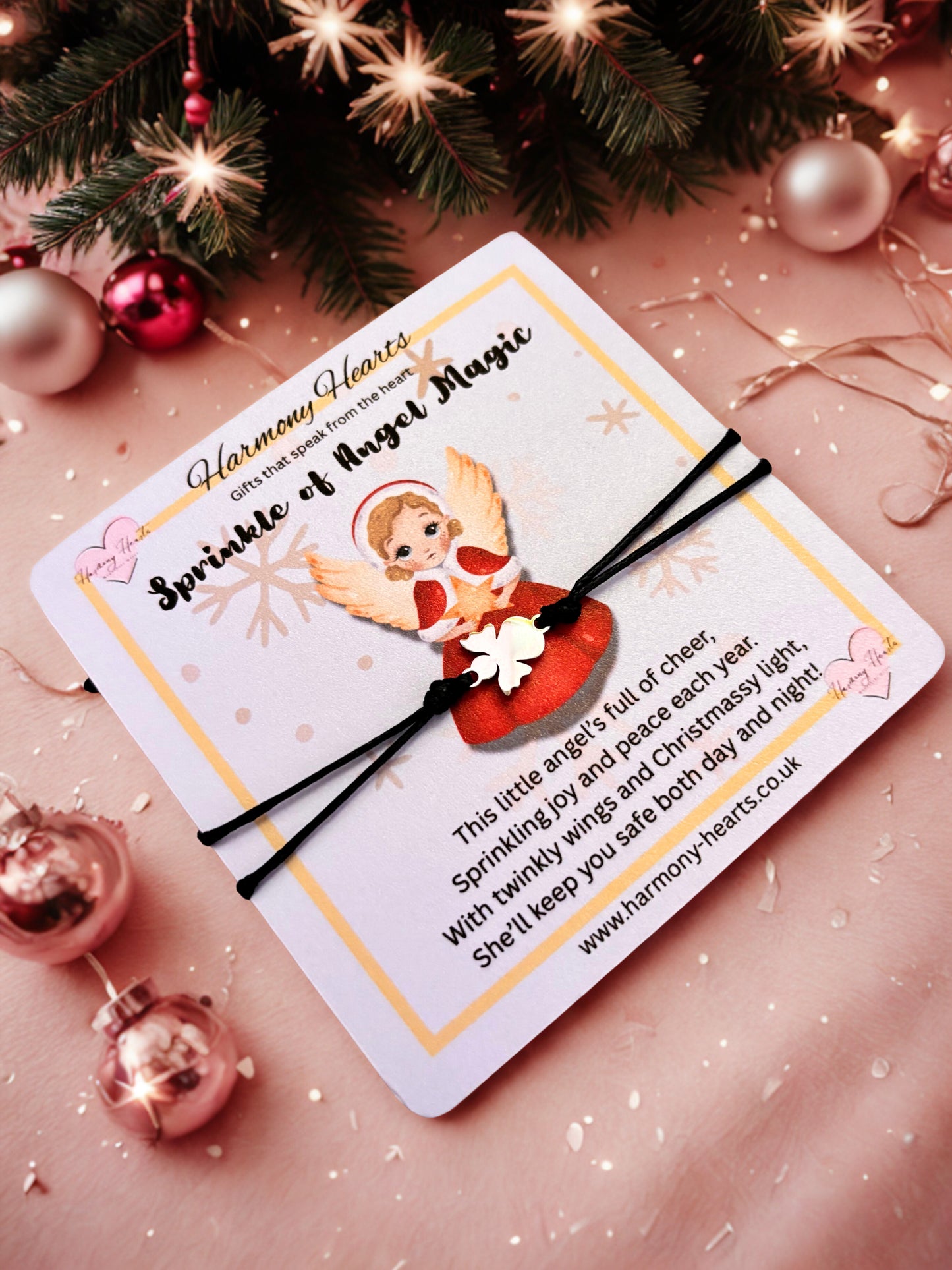 Bracelet on a card with angel design and text, surrounded by Christmas decorations on a pink background