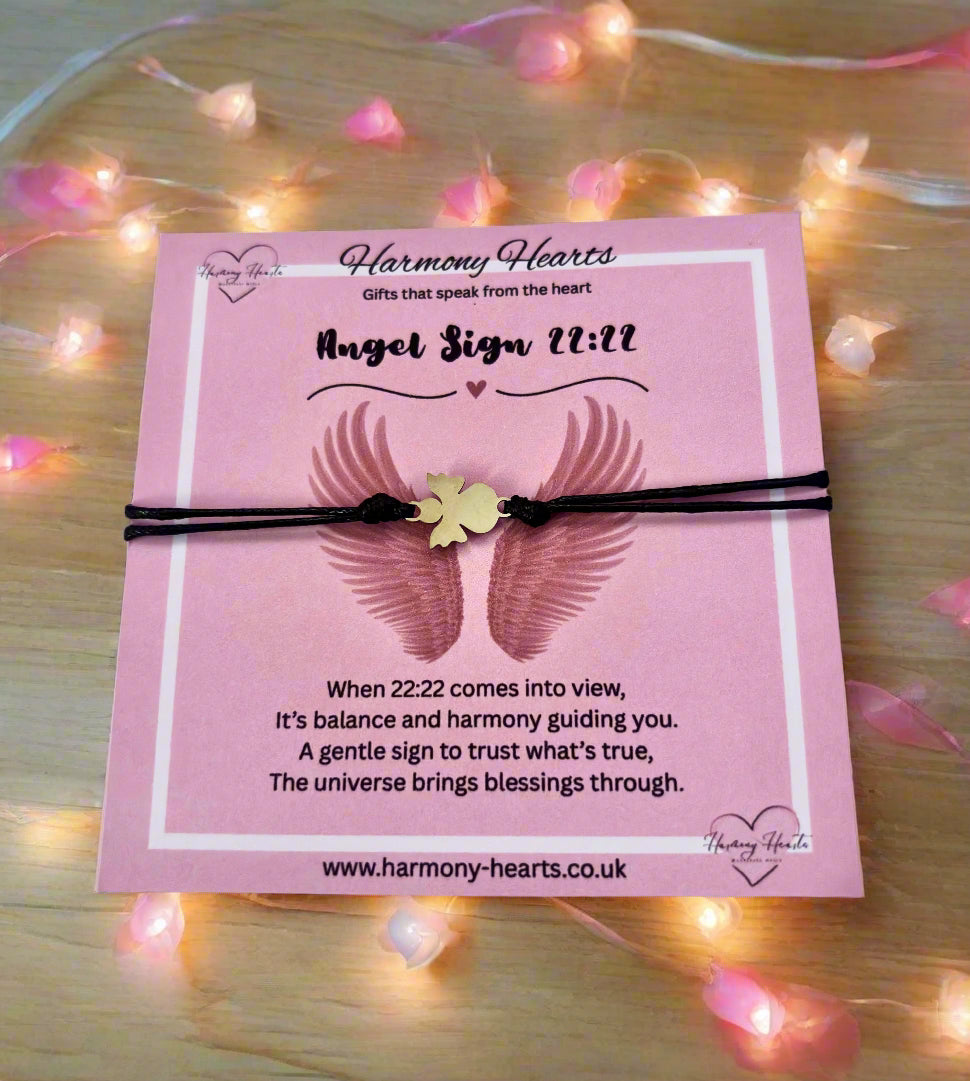 Pink card with angel wings and bracelet on a wooden surface with fairy lights.