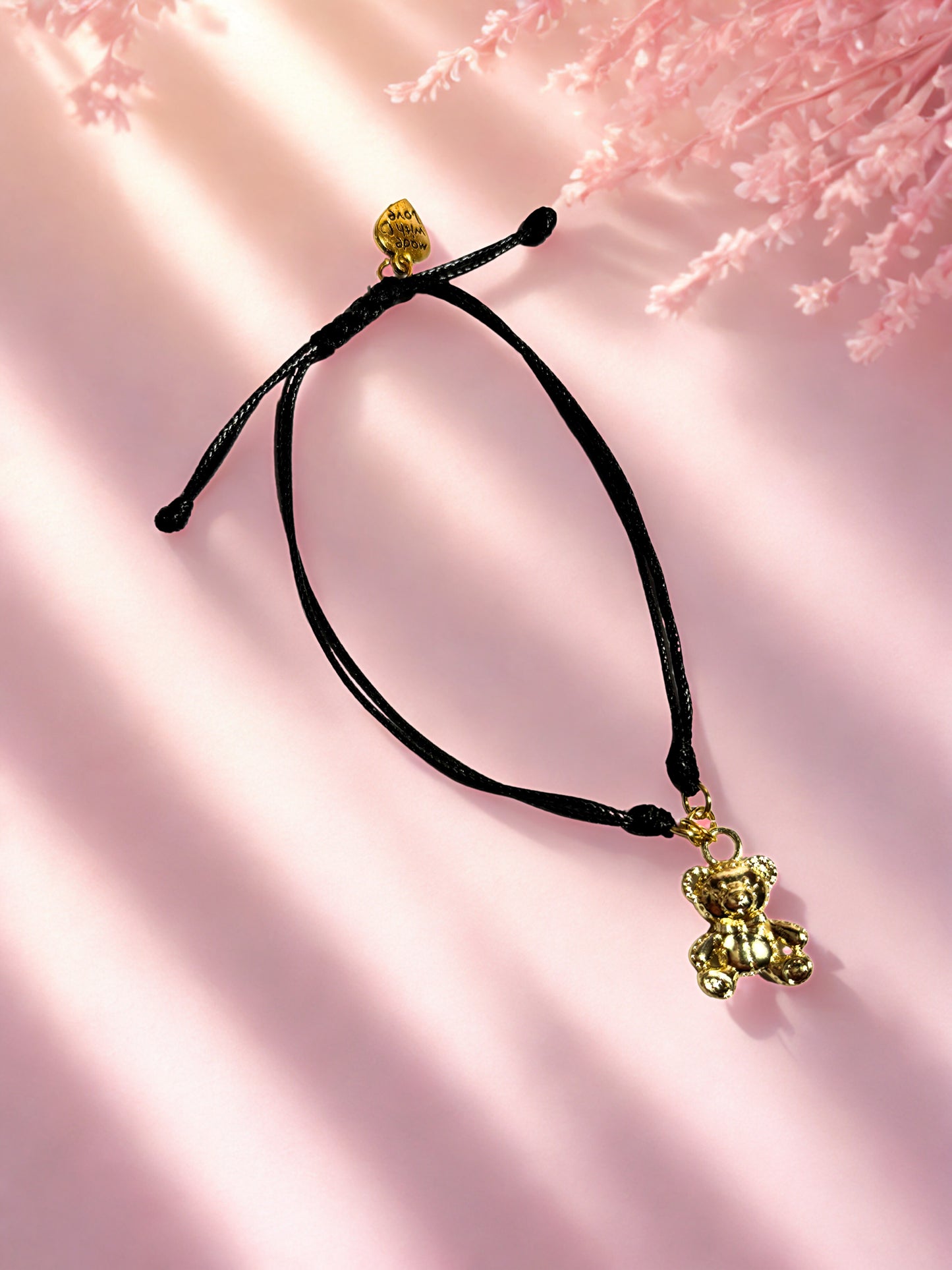 Black cord bracelet with gold bear charm on a pink background