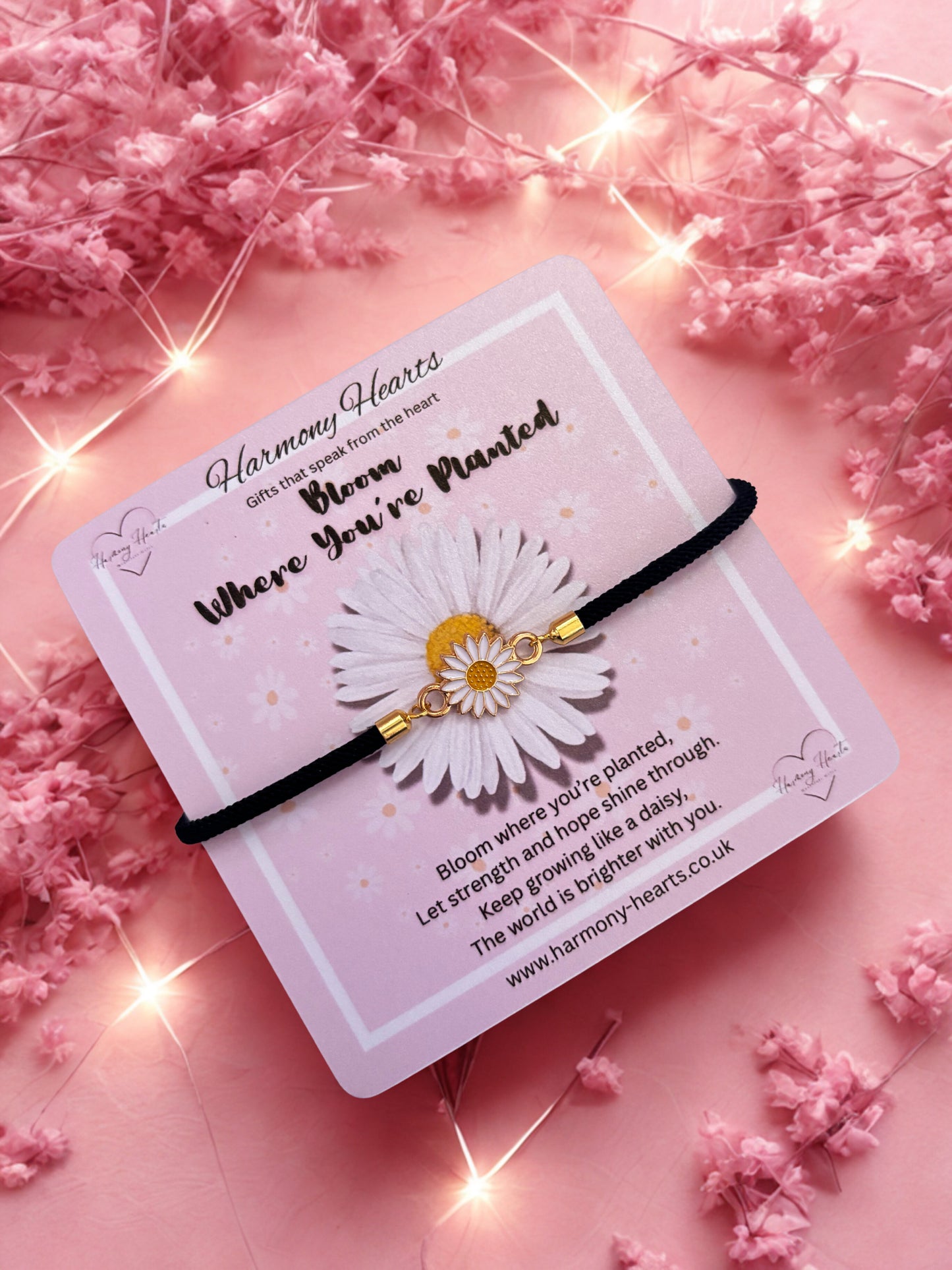 Daisy bracelet on a card with pink flowers and lights in the background