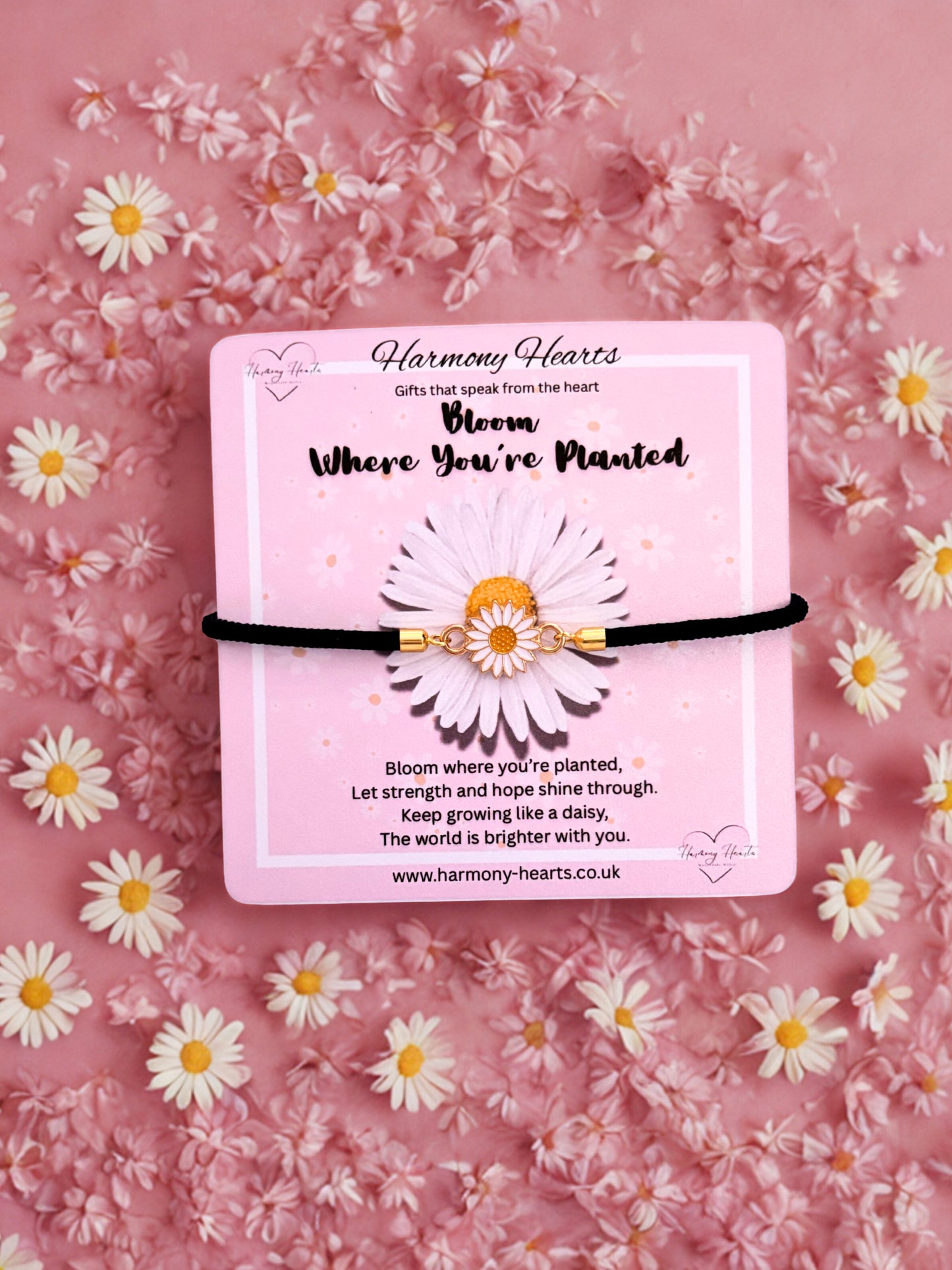 Black cord bracelet with daisy design on a pink card with floral background