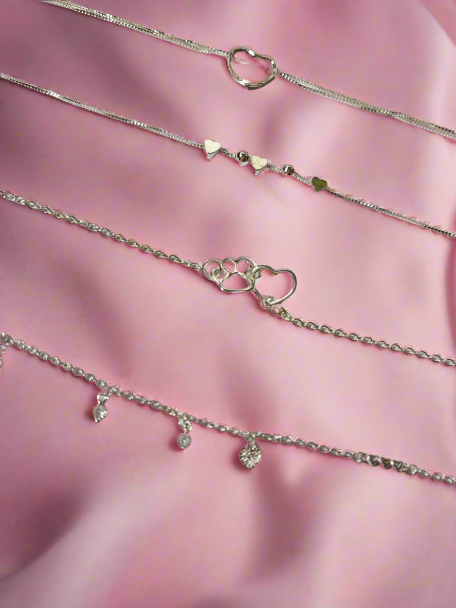 Set of silver bracelets with heart and paw print charms on a pink fabric background
