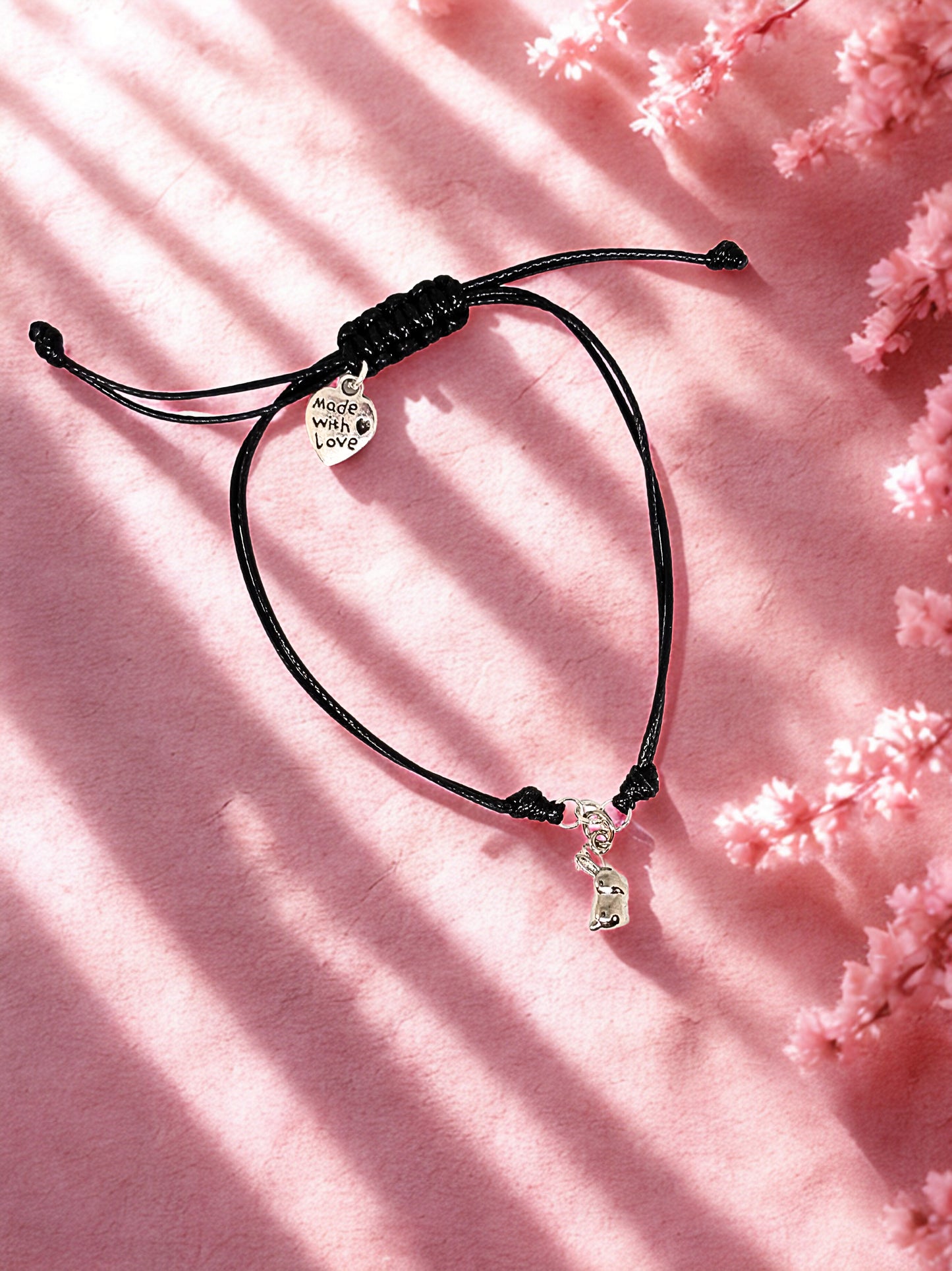 Black cord bracelet with a silver bunny charm on a pink floral background