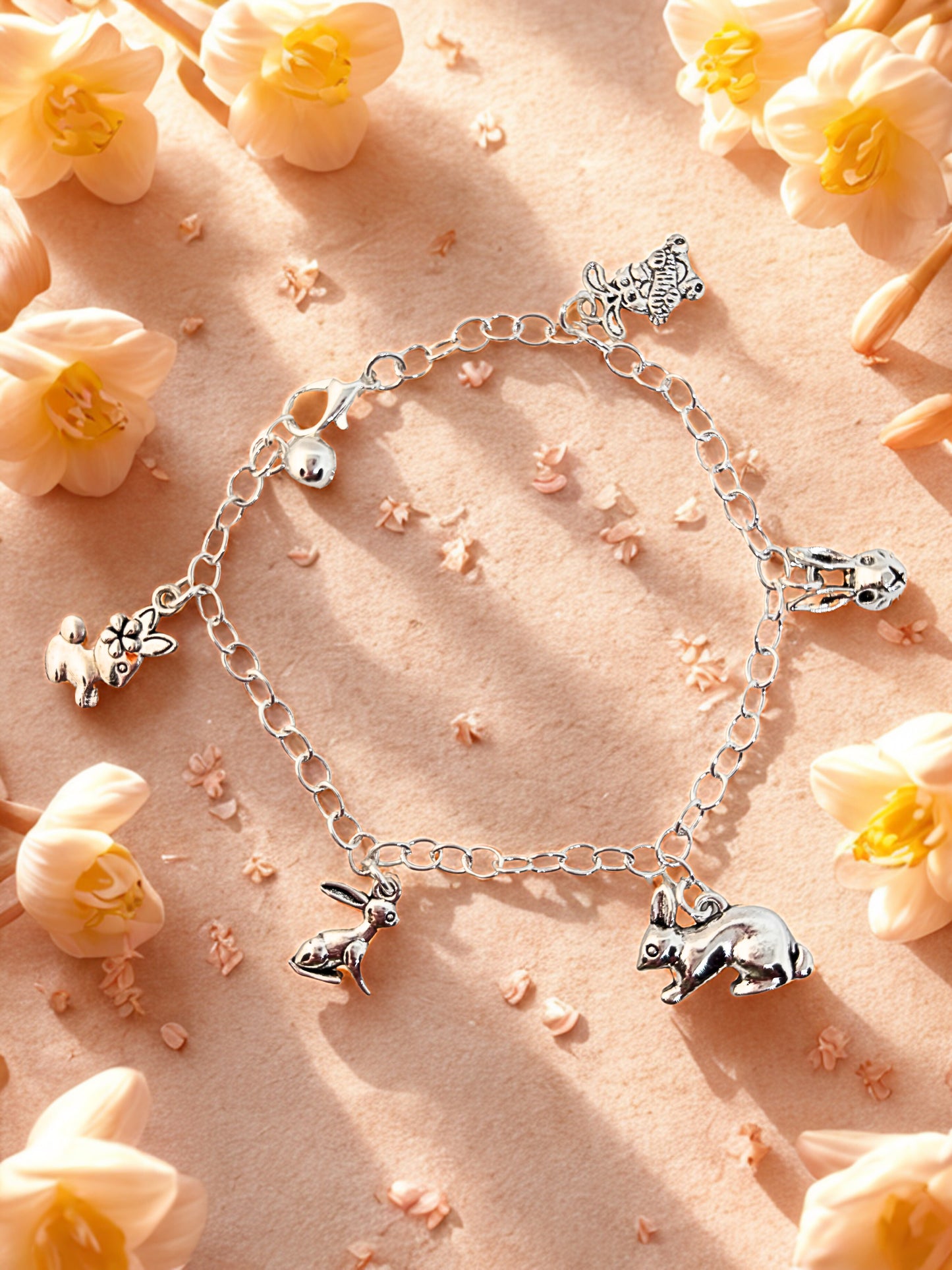 Silver bracelet with bunny charms on a pink background with flowers