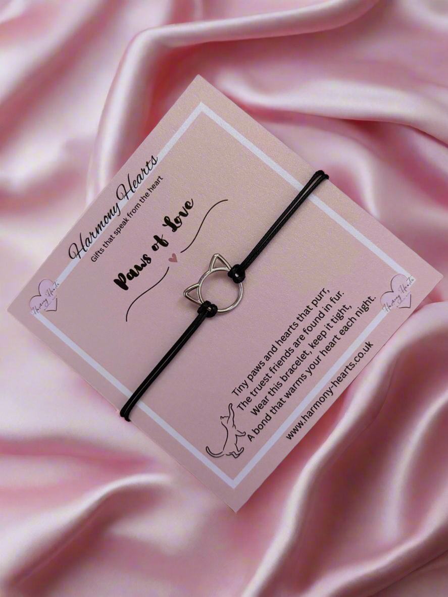 Black cat-shaped bracelet on a pink card with 'Harmony Hearts' branding against a pink satin background