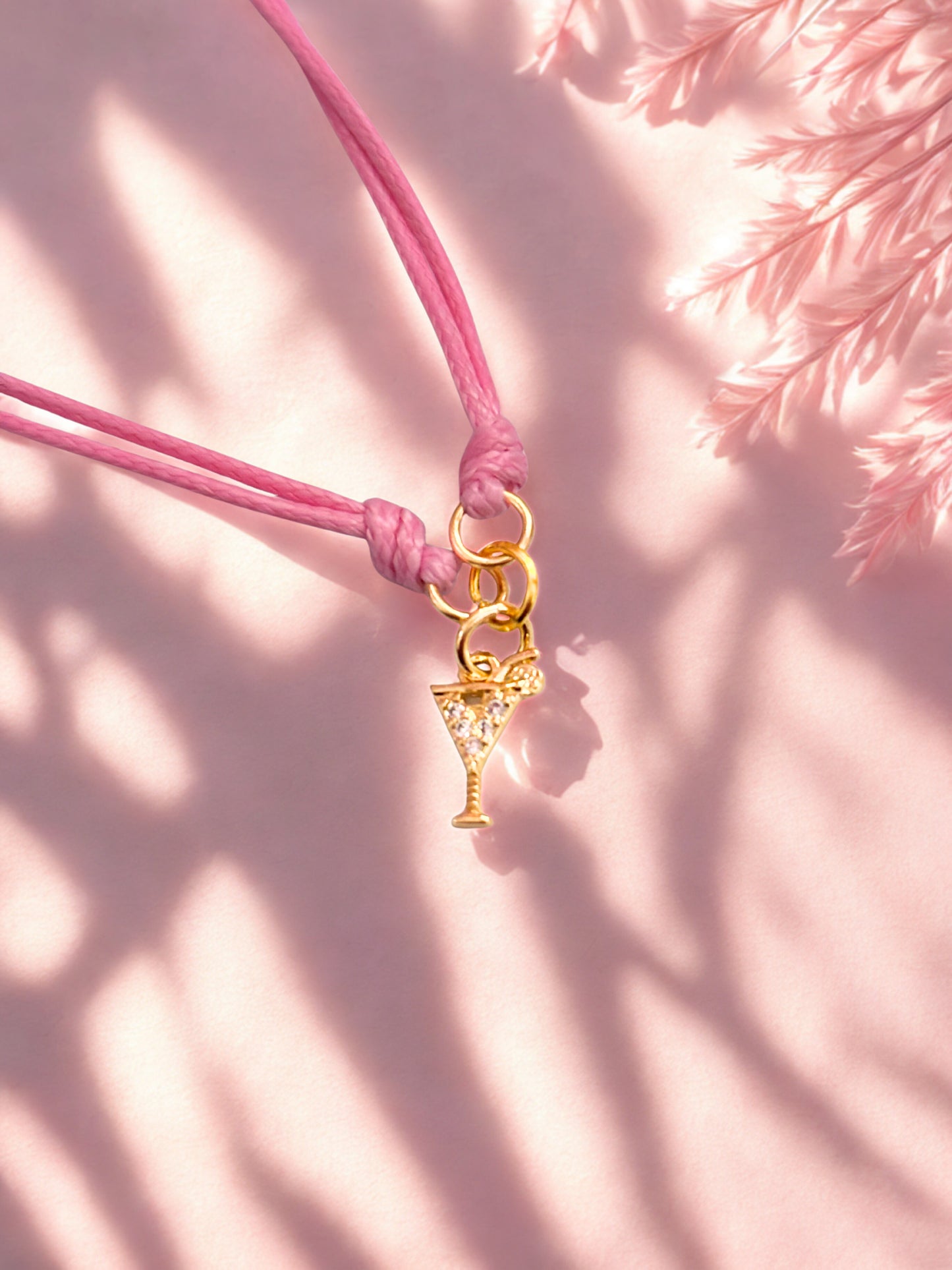 Pink cord bracelet with a gold cocktail charm on a pink background