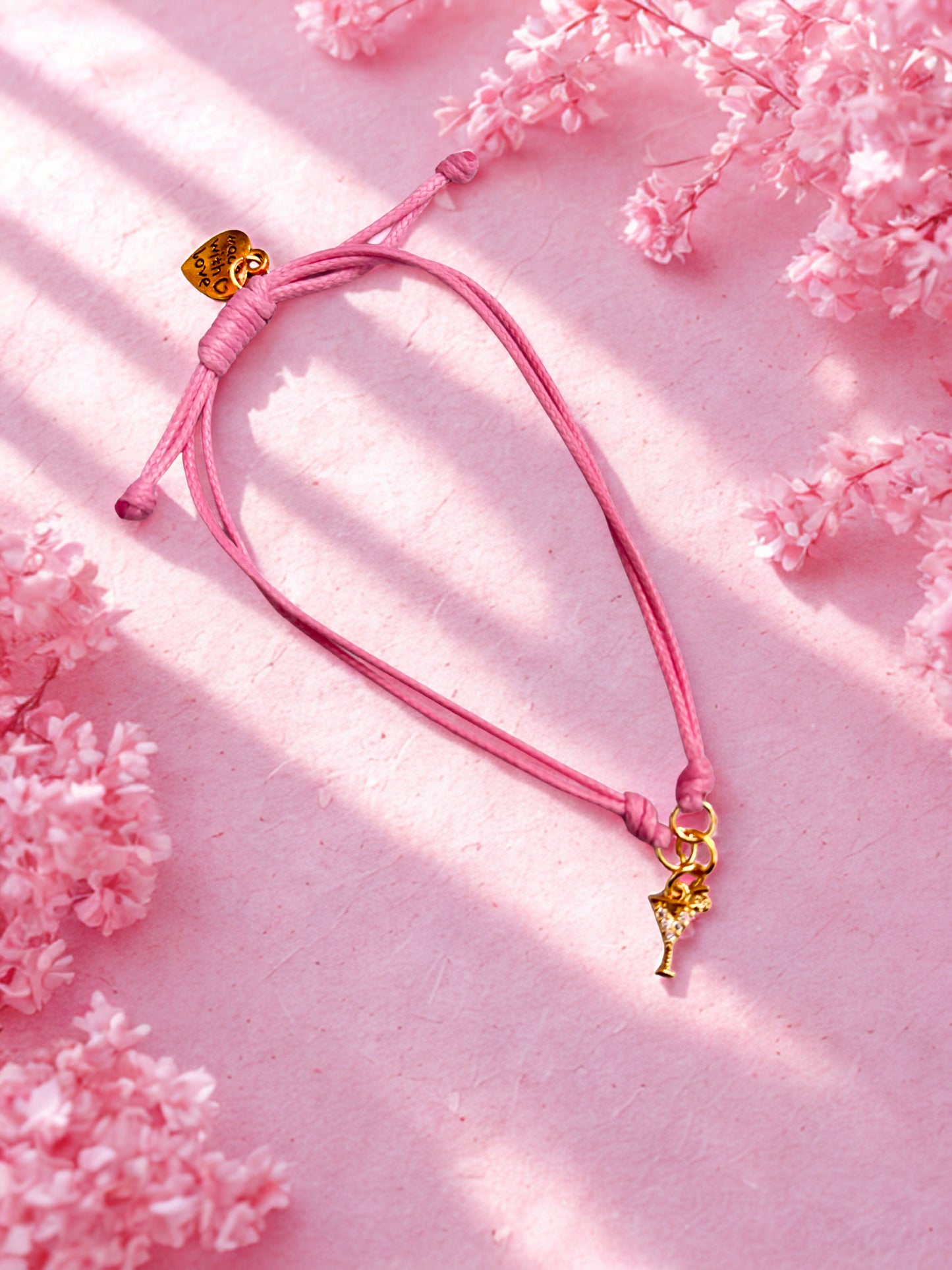 Pink bracelet with a gold cocktail charm on a pink floral background