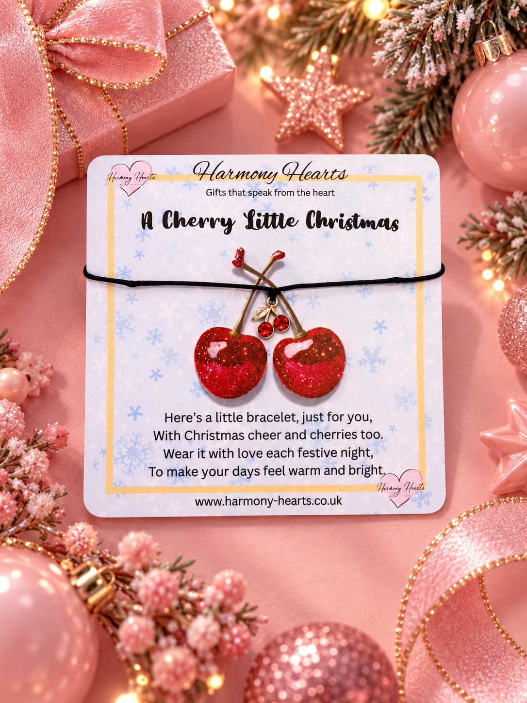 A branded card by Harmony Hearts with a Cherry Charm wish bracelet on a black cord set against a pink festive background