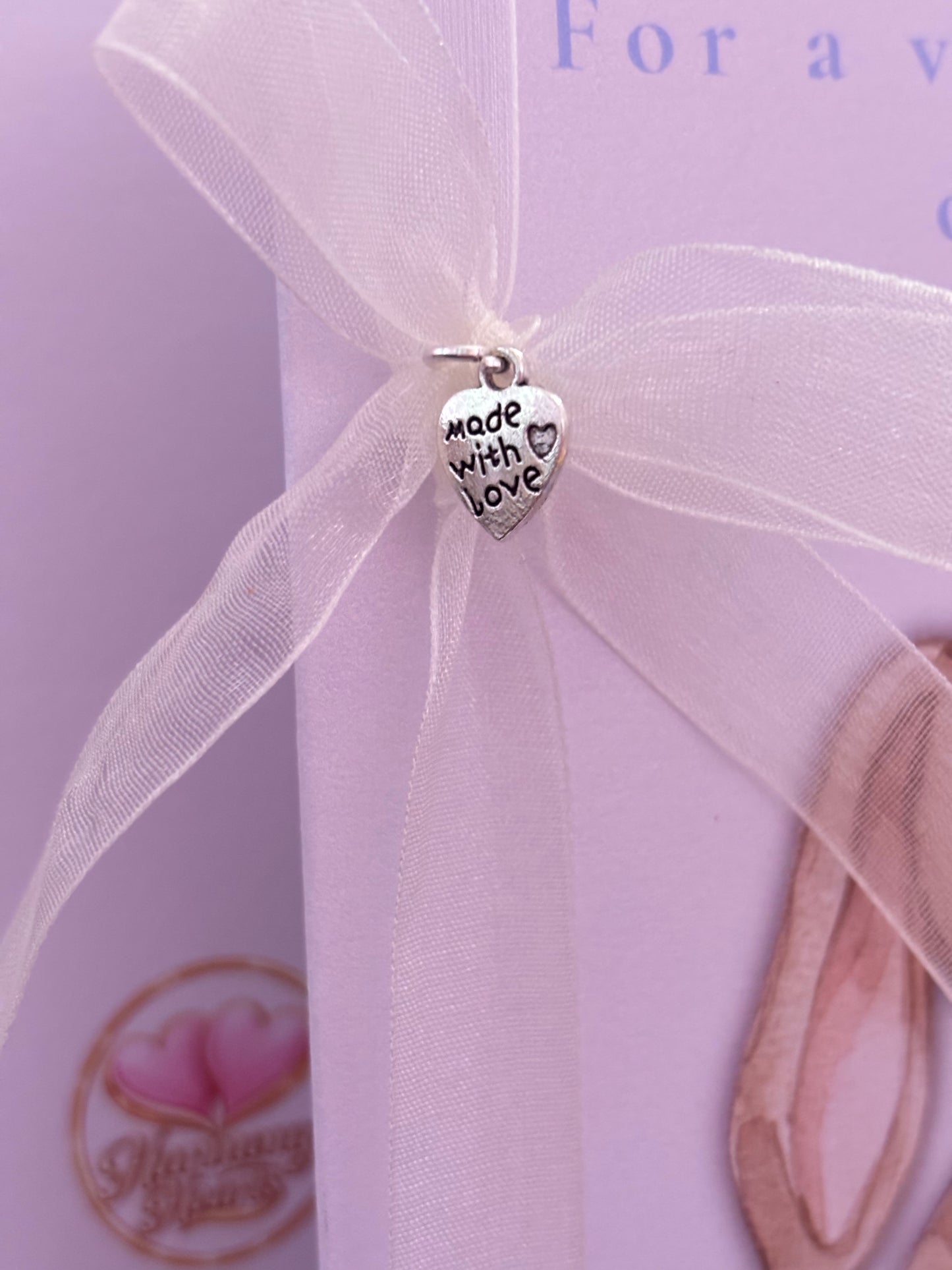 Heart-shaped 'made with love' charm on a silver ribbon.