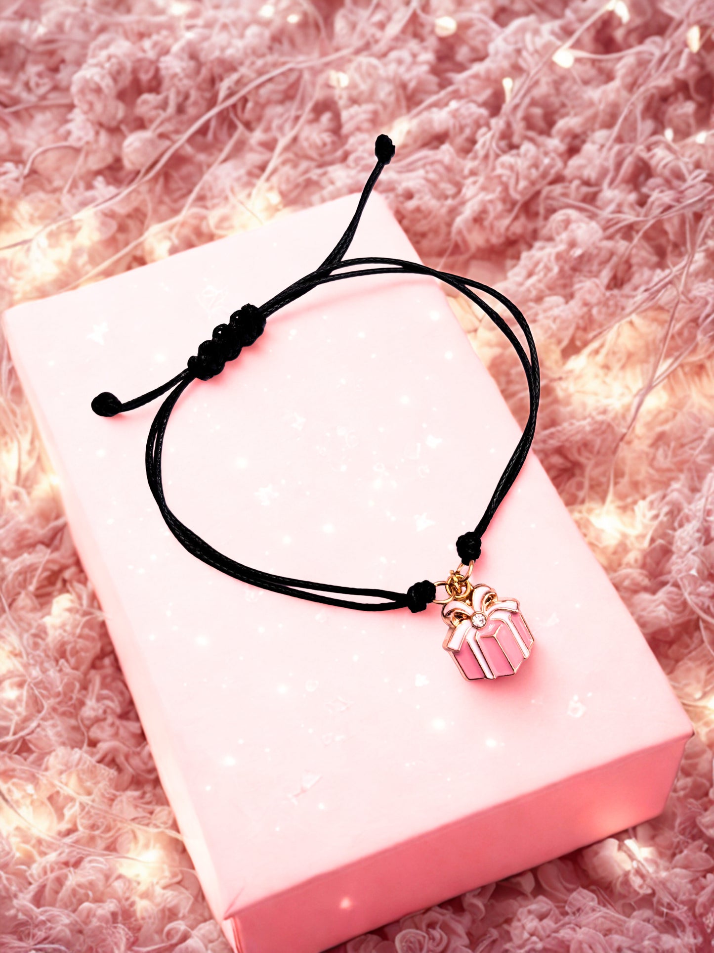 Black cord bracelet with a pink gift box charm on a pink box against a soft pink background