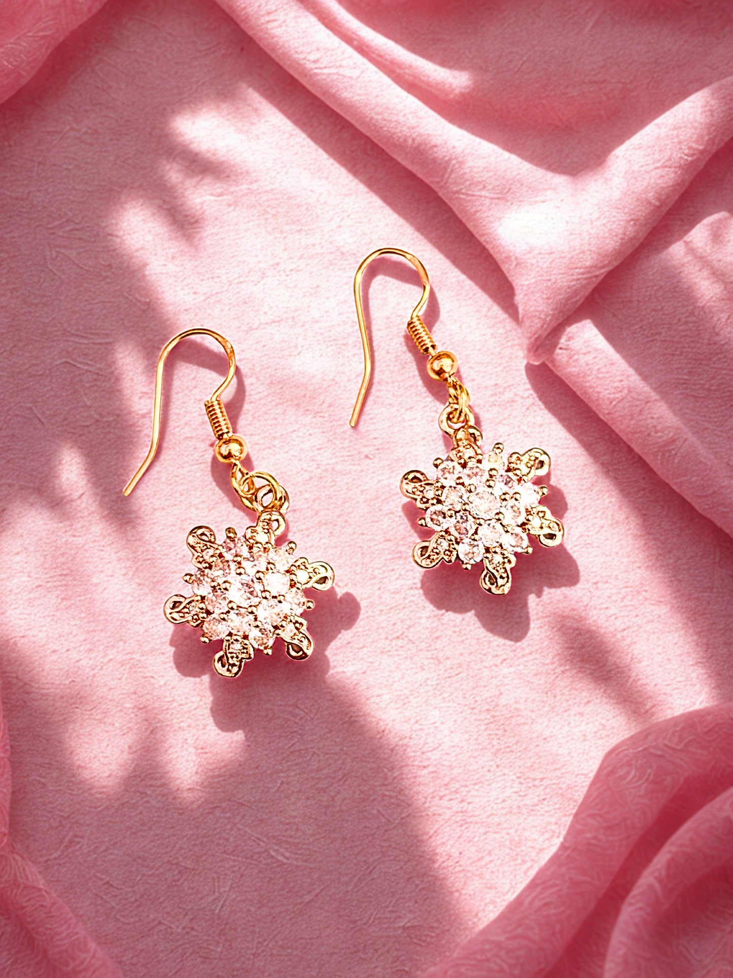 Gold snowflake earrings on a pink fabric background