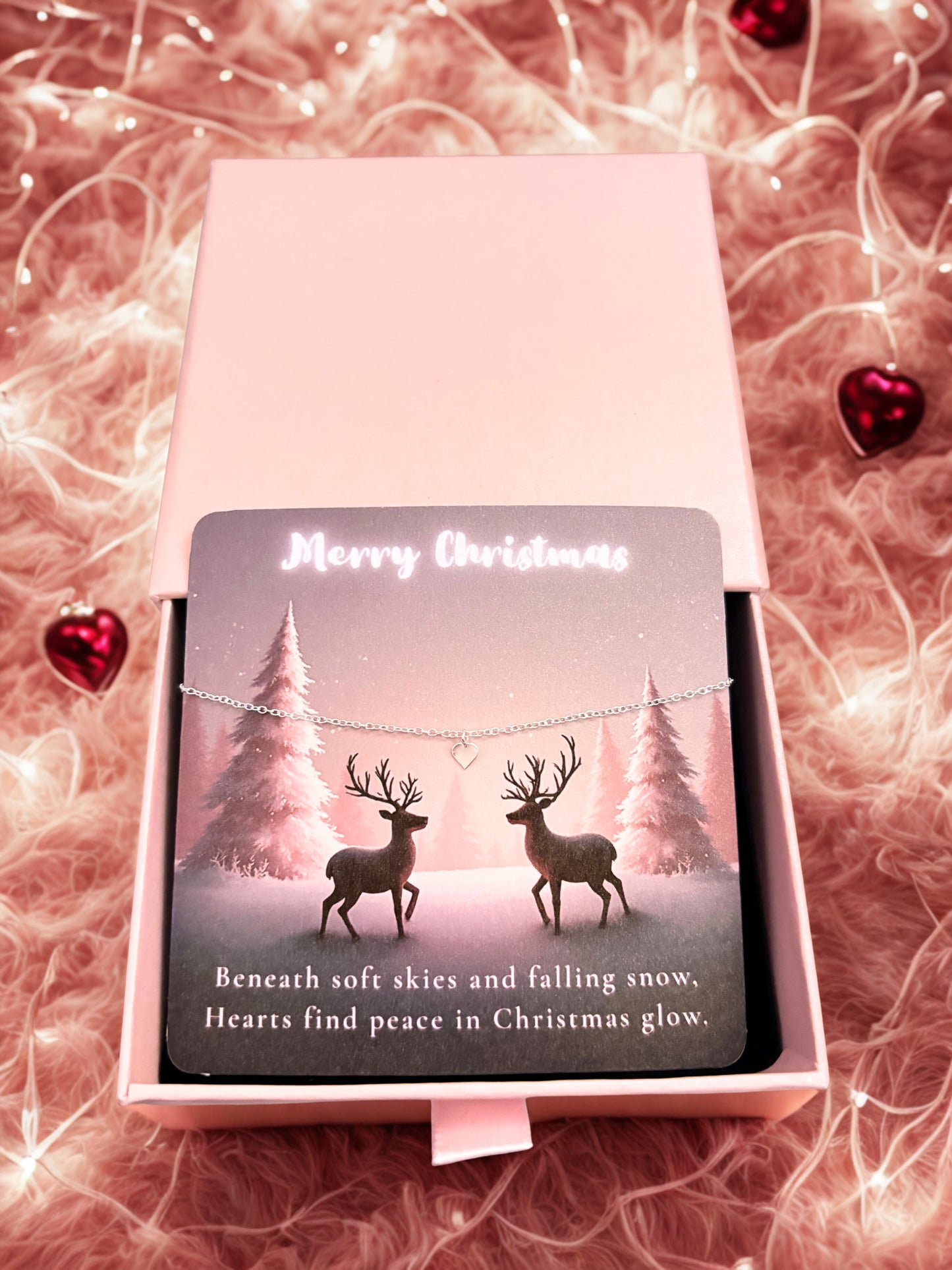 Silver heart bracelet on a Christmas-themed card with deer design in a decorative box on a soft pink background.