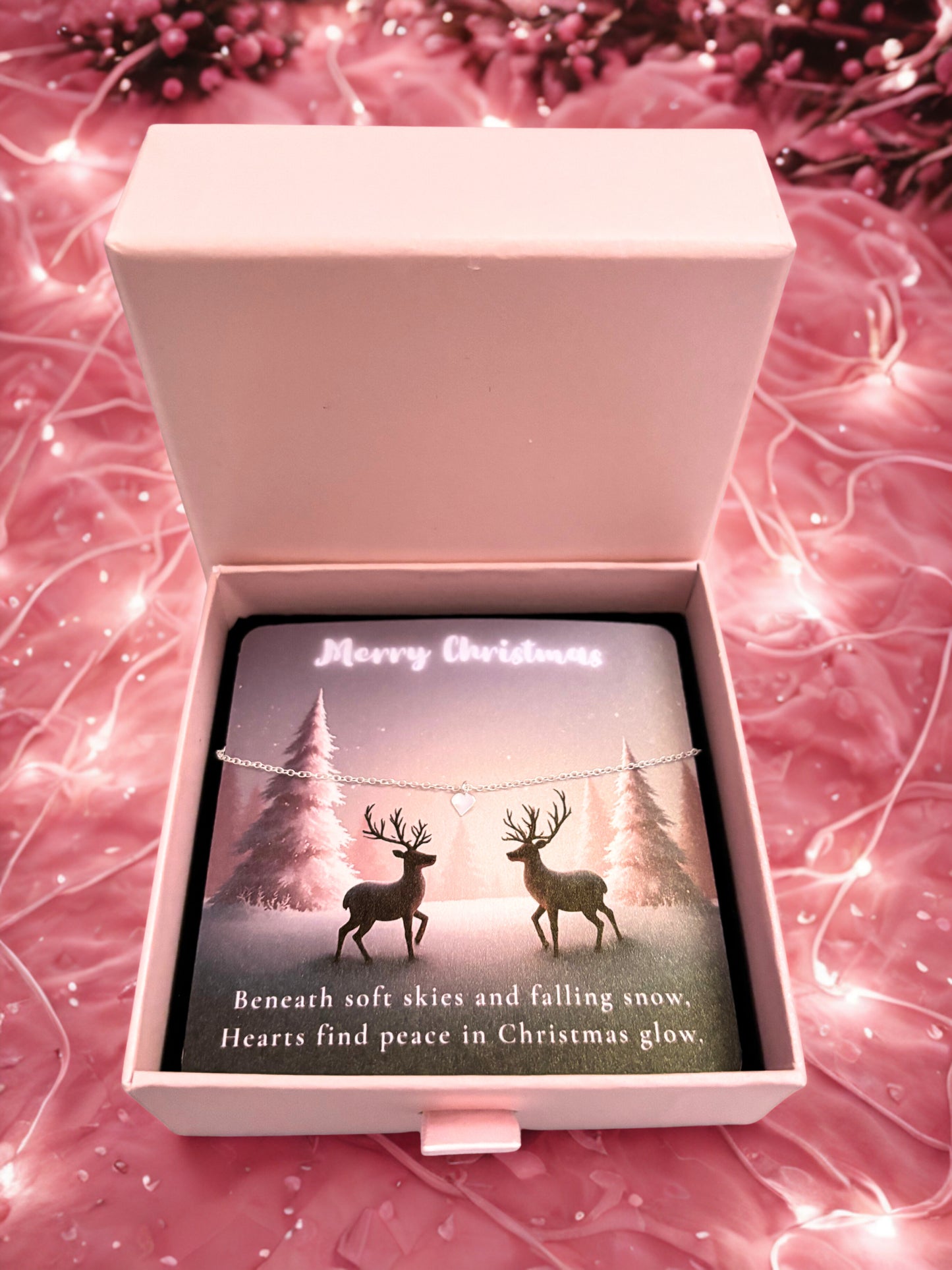 Open pink jewellery box with a silver heart bracelet on a Christmas-themed card on a pink textured background.