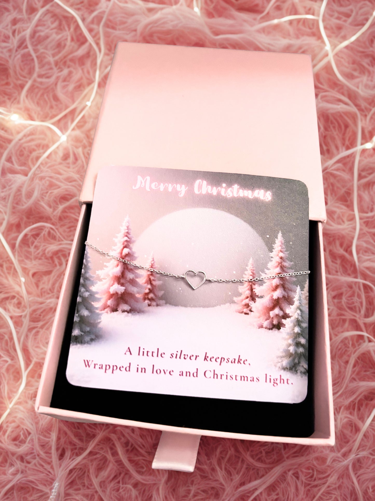 Bracelet with heart charm in a Christmas-themed box on a pink textured background