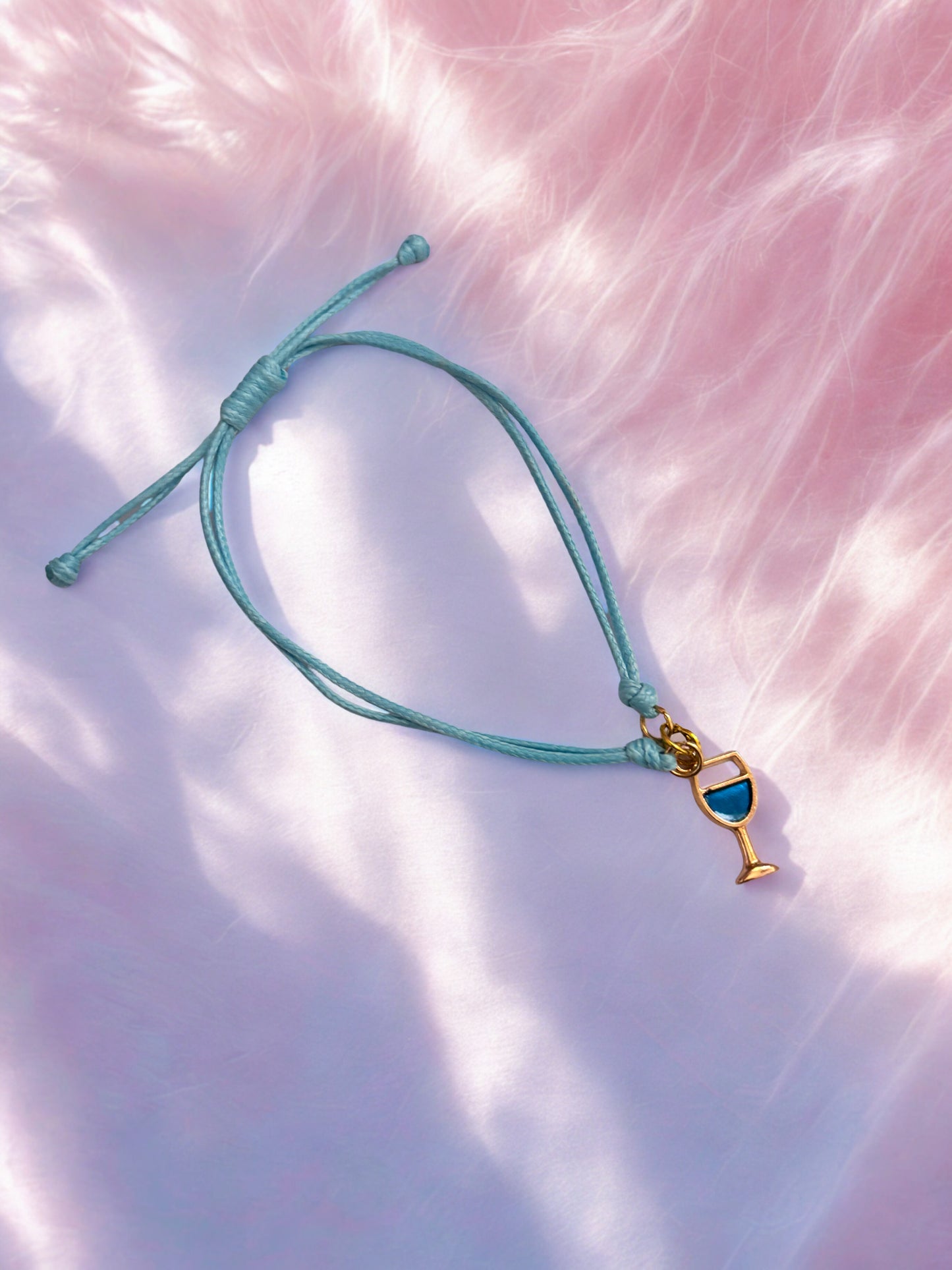 Turquoise bracelet with a gold and blue wine glass charm on a pink textured background