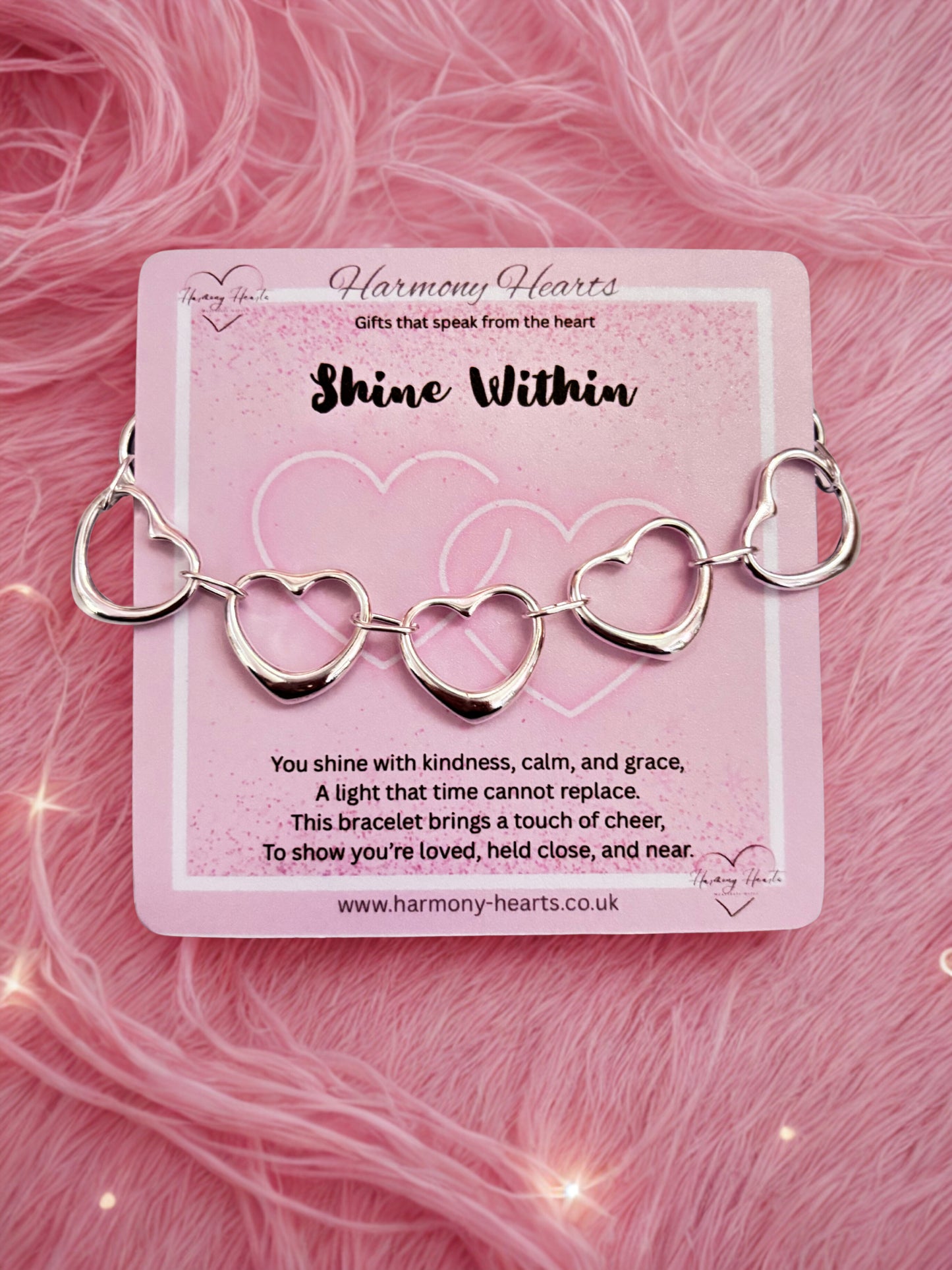 Silver heart-shaped bracelet on a pink card with 'Harmony Hearts' branding against a pink textured background.