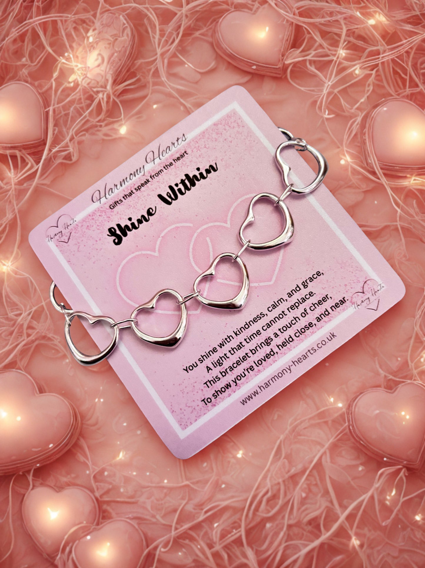 Silver heart-shaped bracelet on a pink card with decorative hearts and lights in the background