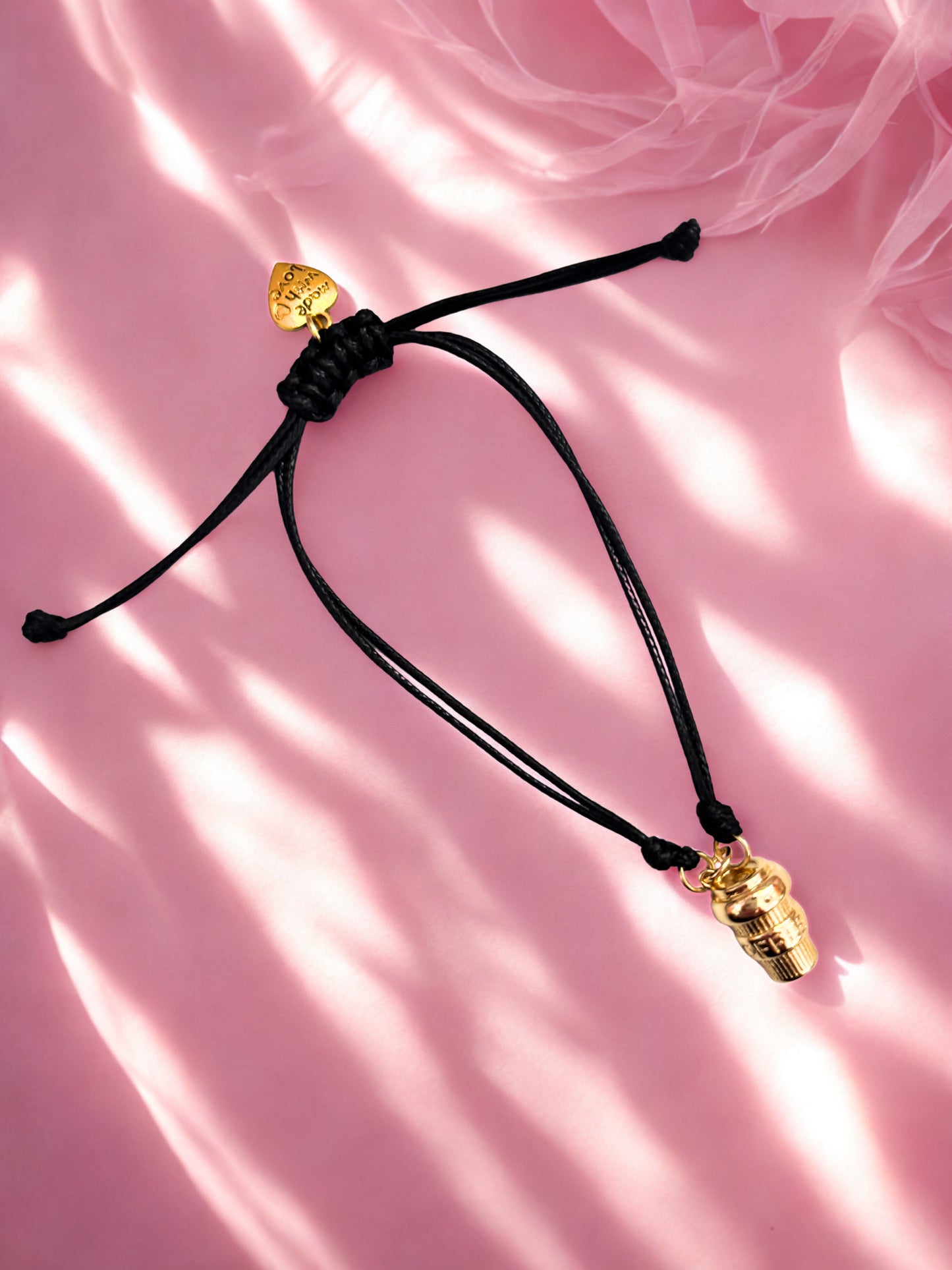 Black cord bracelet with gold coffee cup charm on a pink background