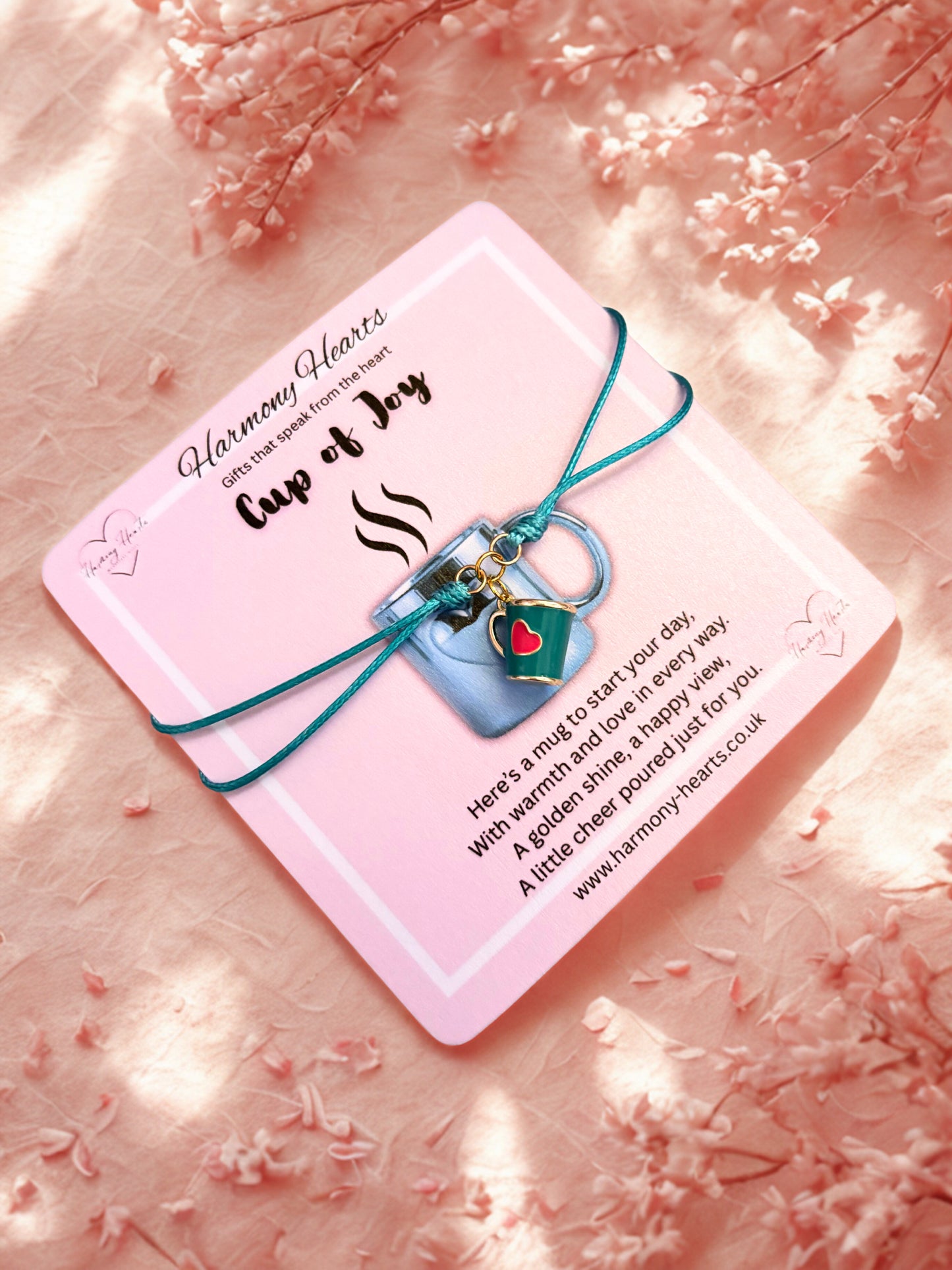 Bracelet with mug charm on a pink card with text, against a soft floral background.