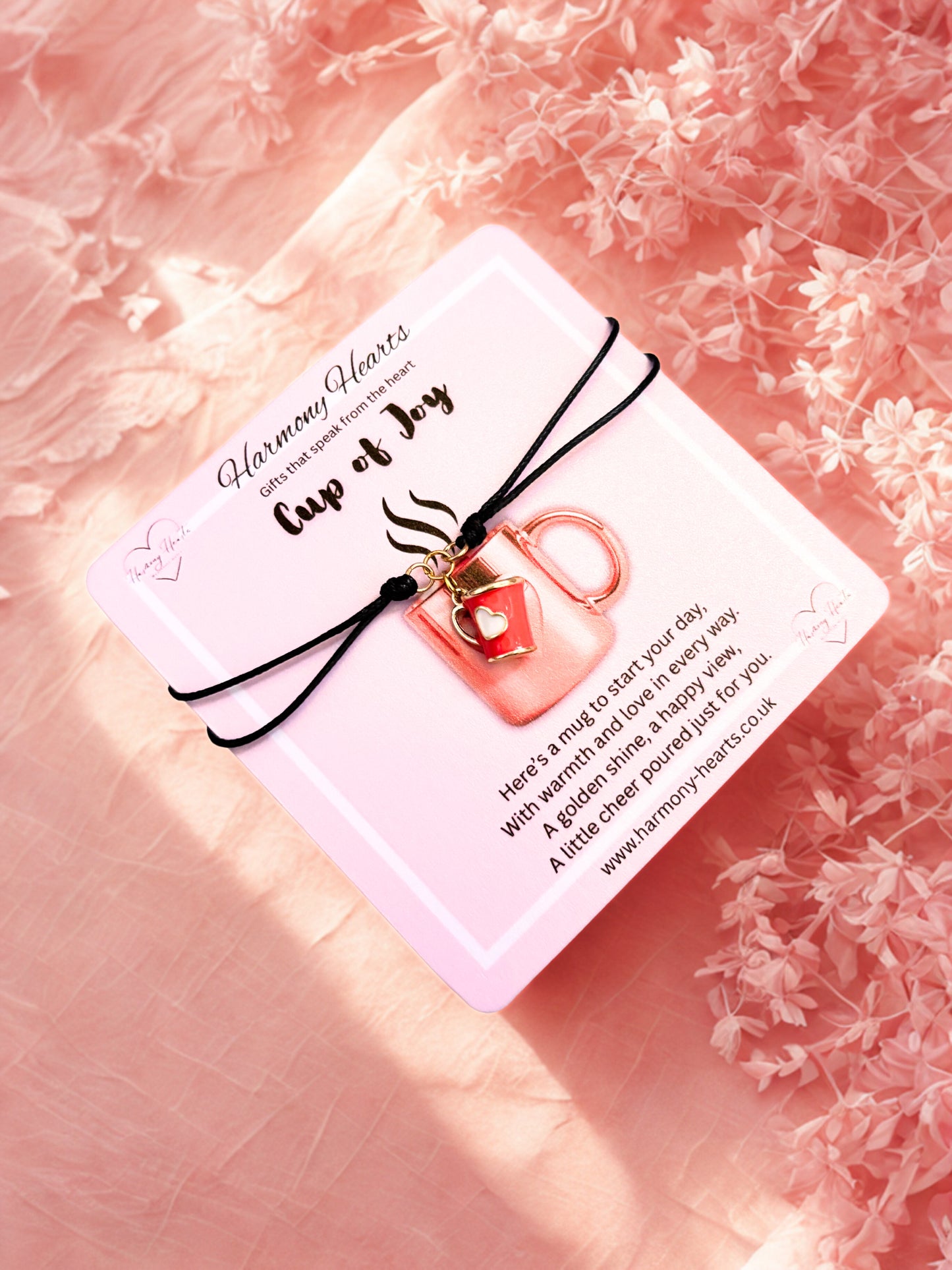 Bracelet with a red mug charm with gold handle on a pink card with text, against a pink floral background