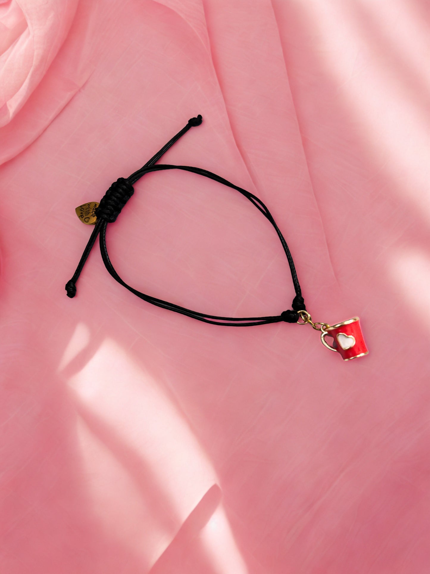 Black cord bracelet with a red cup charm on a pink fabric background