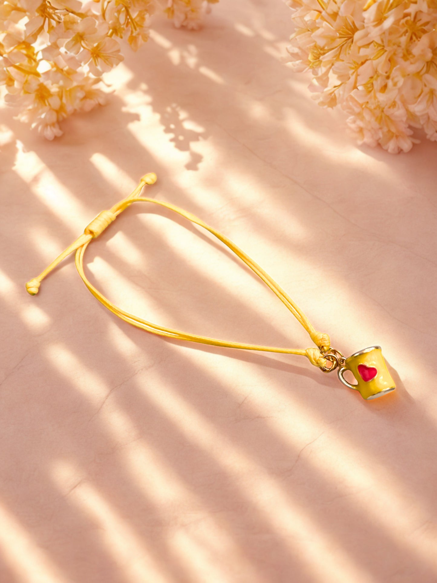 Yellow bracelet with a mug charm on a pink background