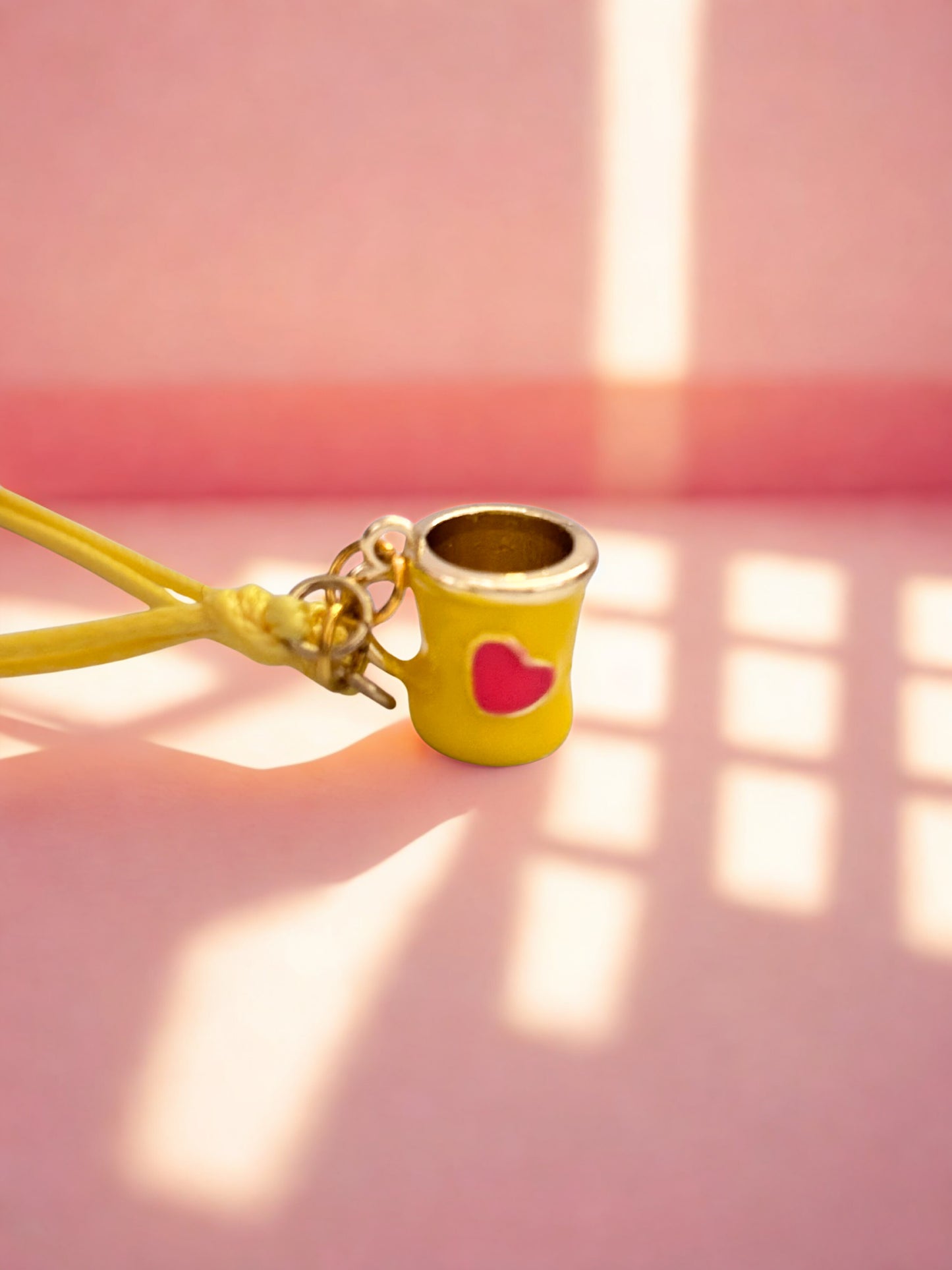 Yellow mug charm with a pink heart on a pink background