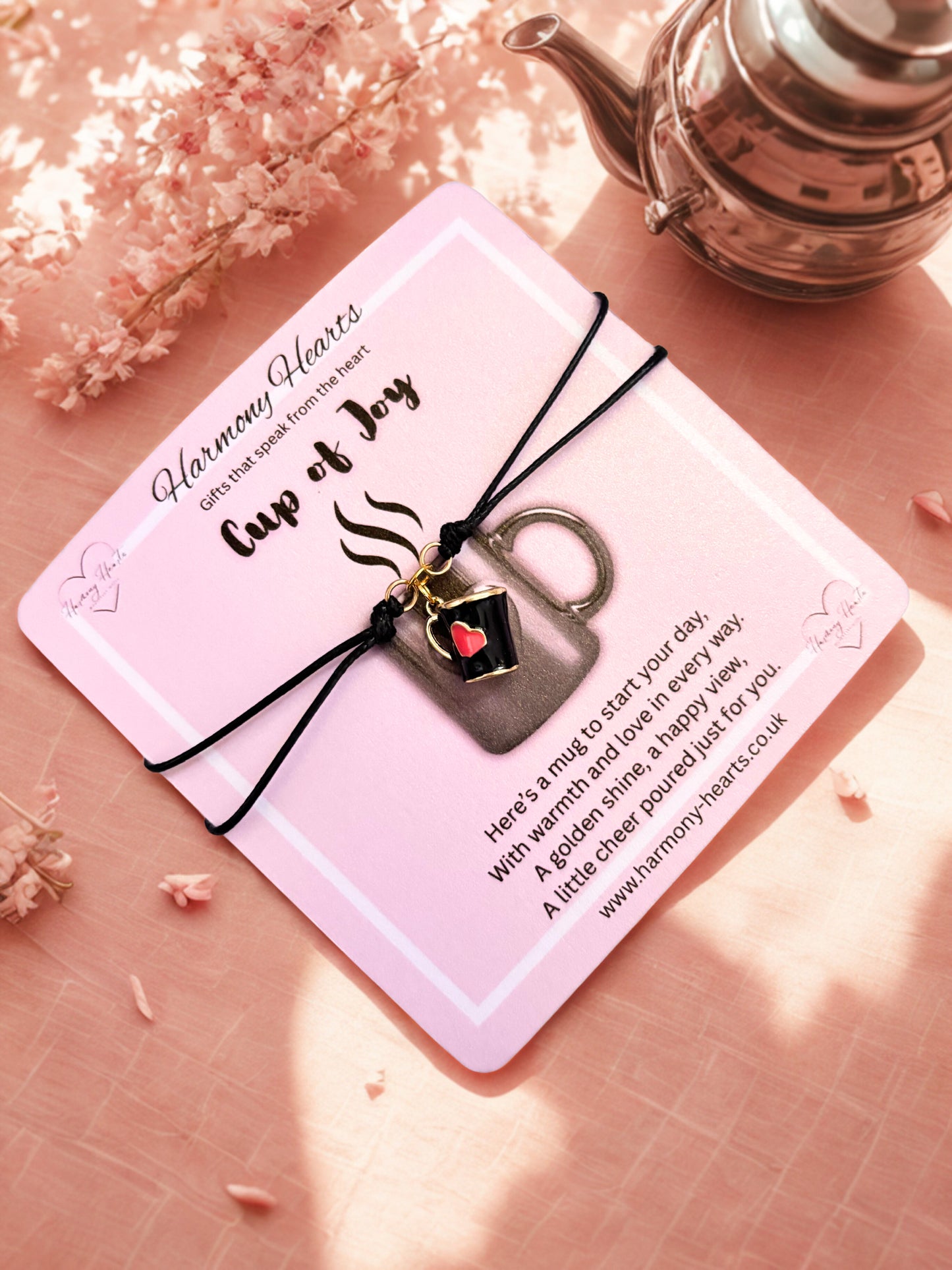 Bracelet with a mug charm on a pink card with decorative elements on a pink surface.