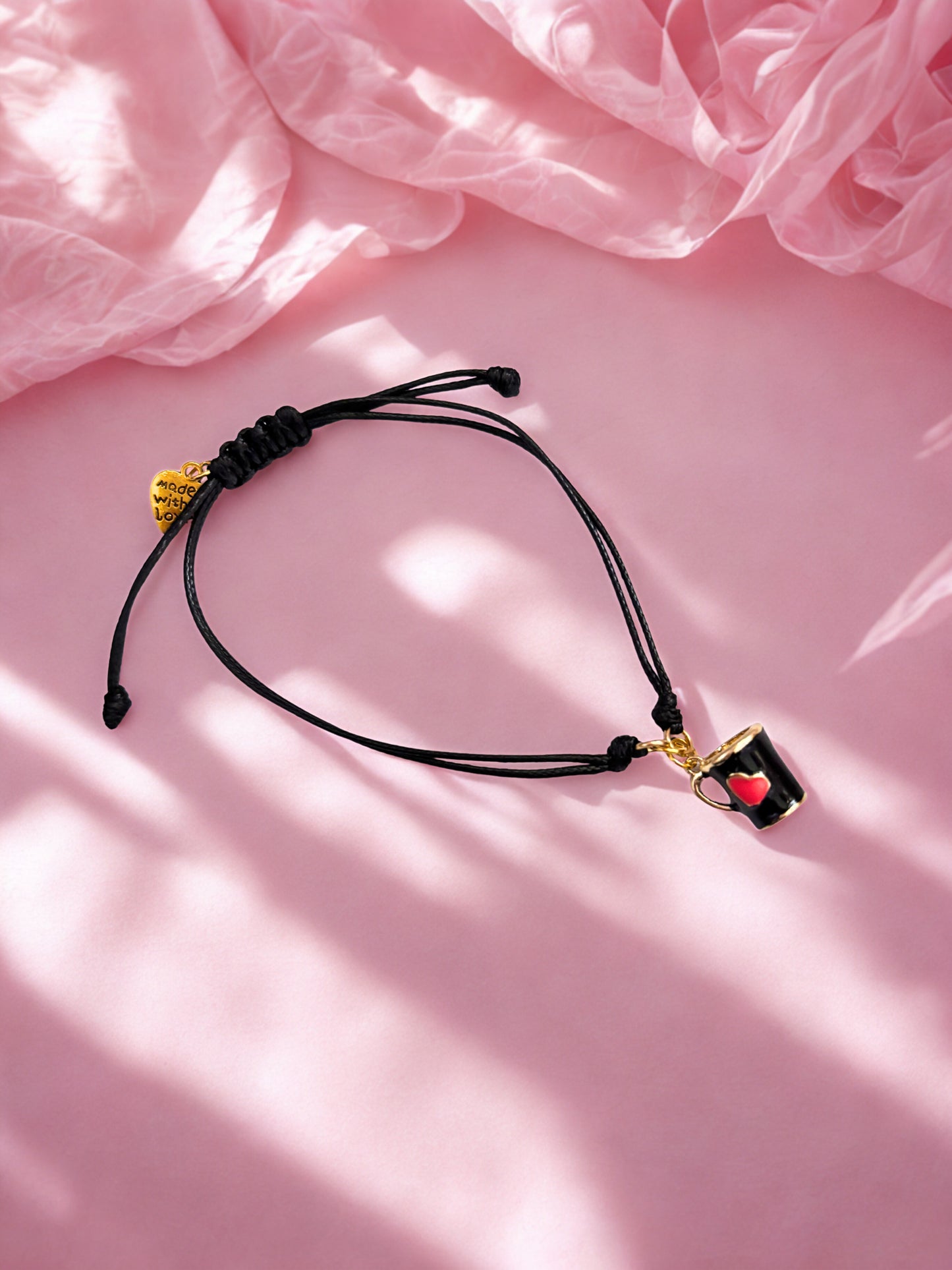 Black cord bracelet with a mug charm on a pink fabric background