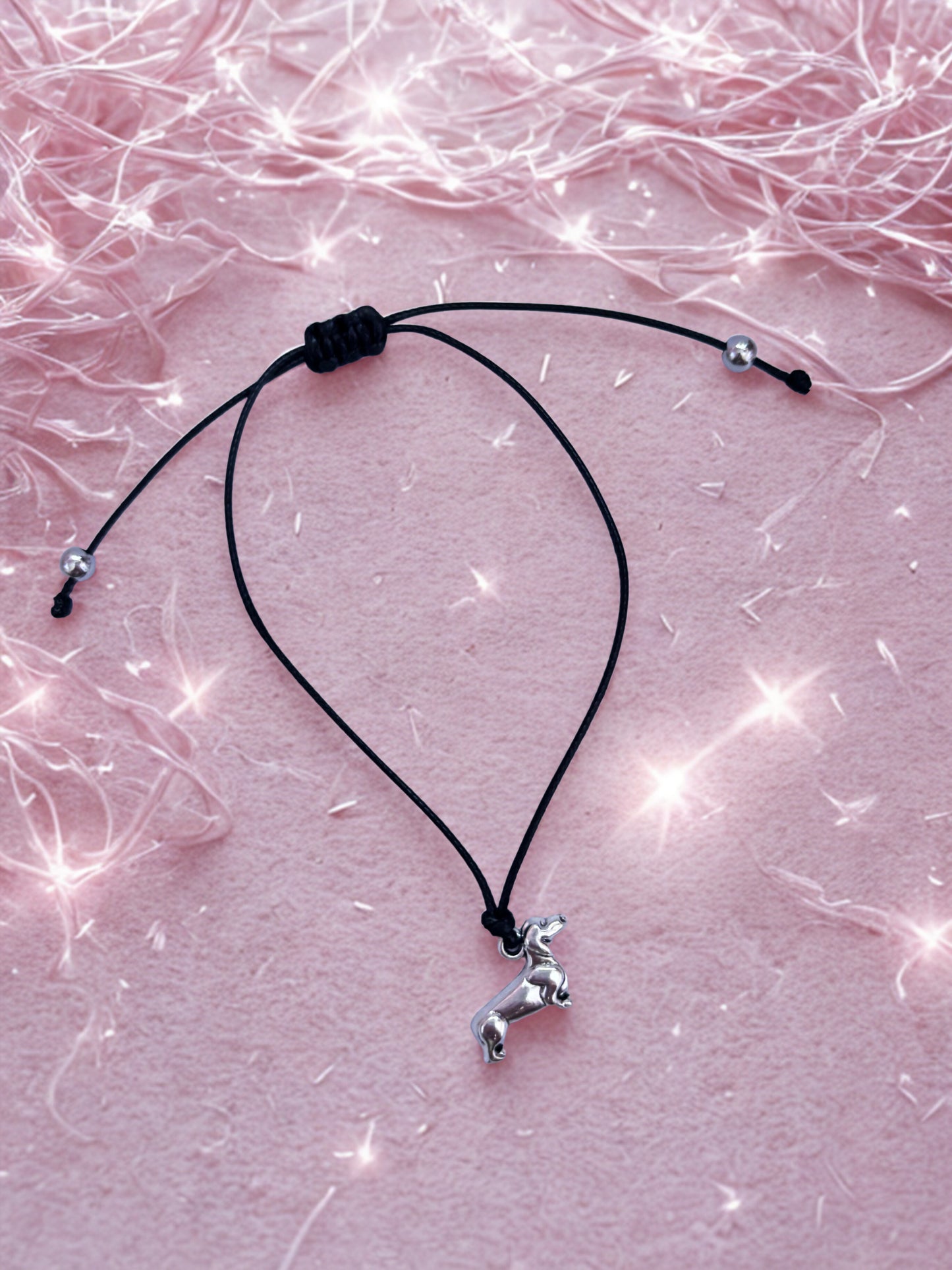 Black cord bracelet with a small silver dachshund dog pendant on a pink textured background