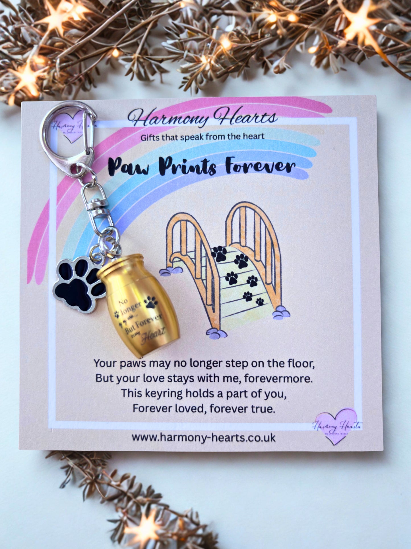 Keychain with gold urn and paw prints on a 'Harmony Hearts' card with decorative lights.
