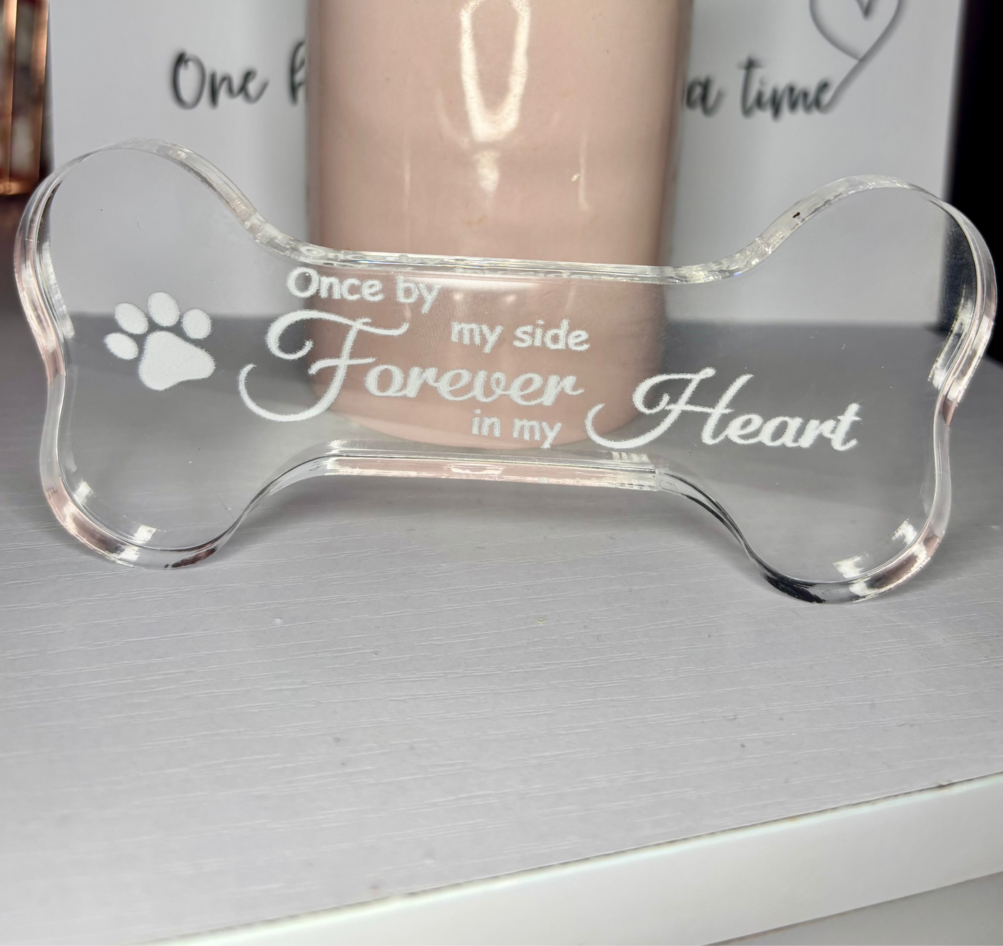 Clear acrylic pet memorial bone with engraved text on a gray surface