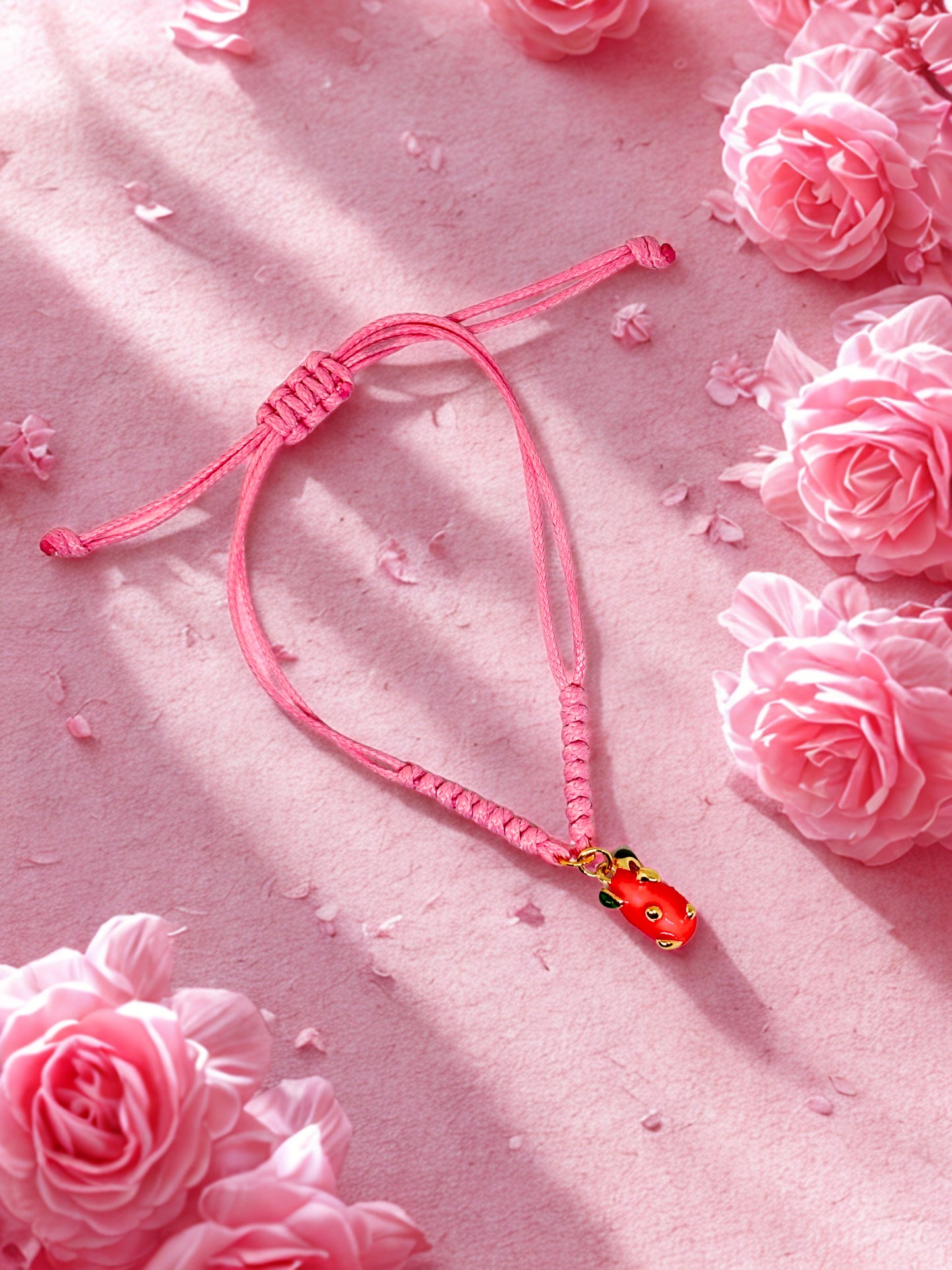 Pink cord bracelet with a pink dragon fruit charm laid on a pink surface