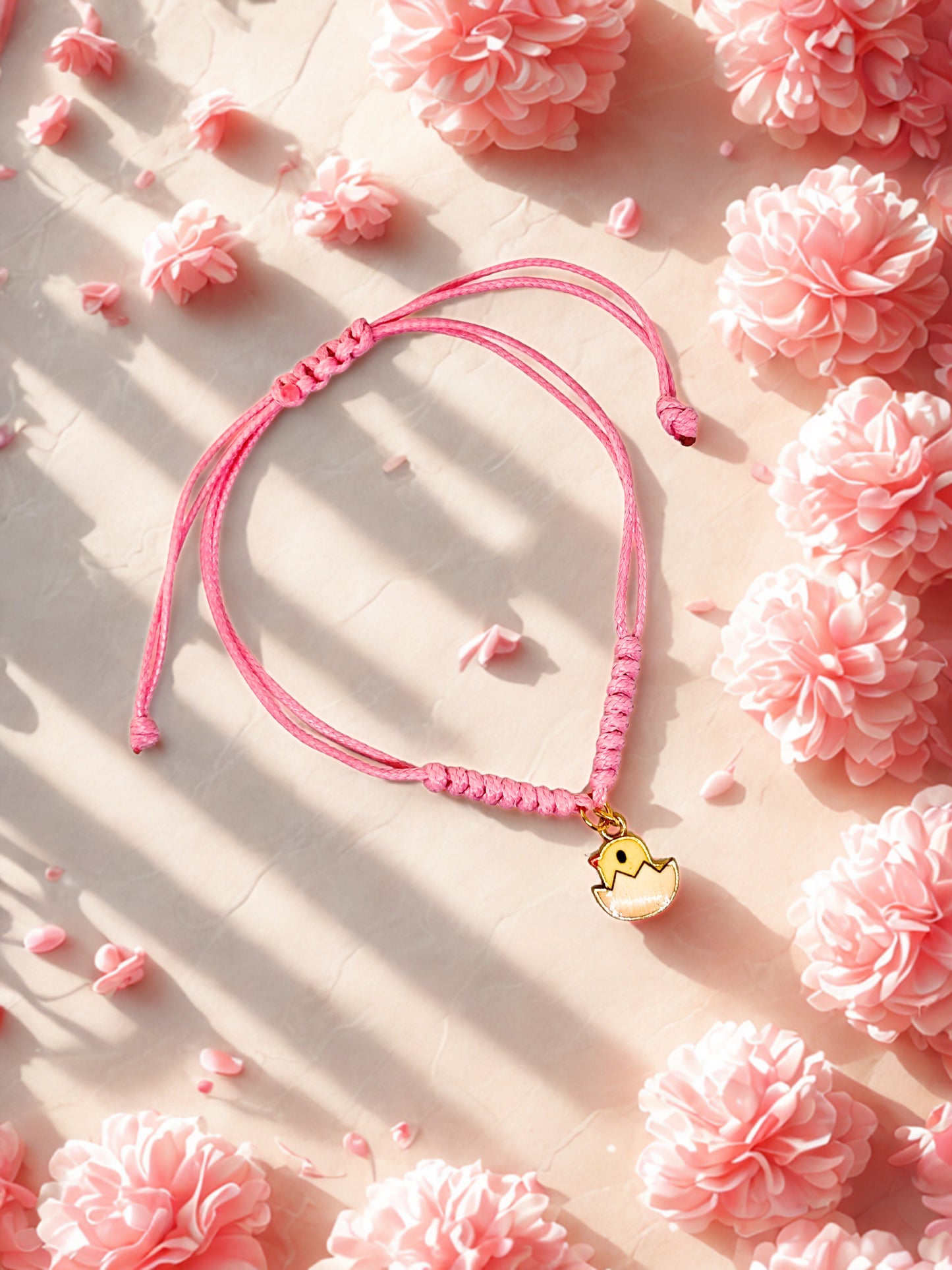 Pink cord bracelet with a small yellow chick charm on a pink floral background