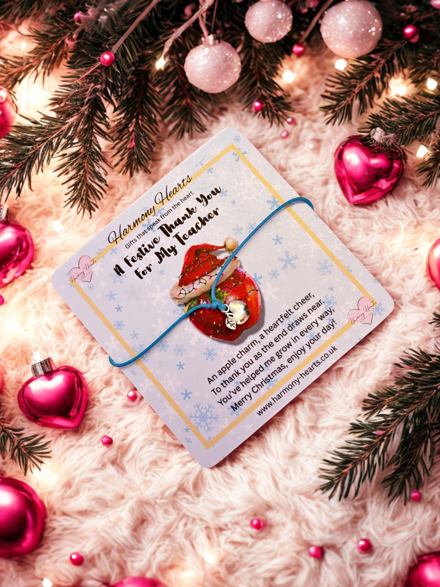 Christmas-themed card with a red apple design and apple charm bracelet surrounded by festive decorations on a soft pink surface.