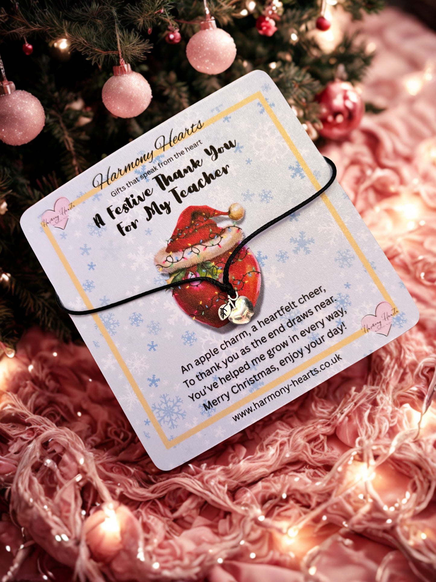 Card with an apple charm bracelet and festive design on a pink textured background with Christmas decorations.