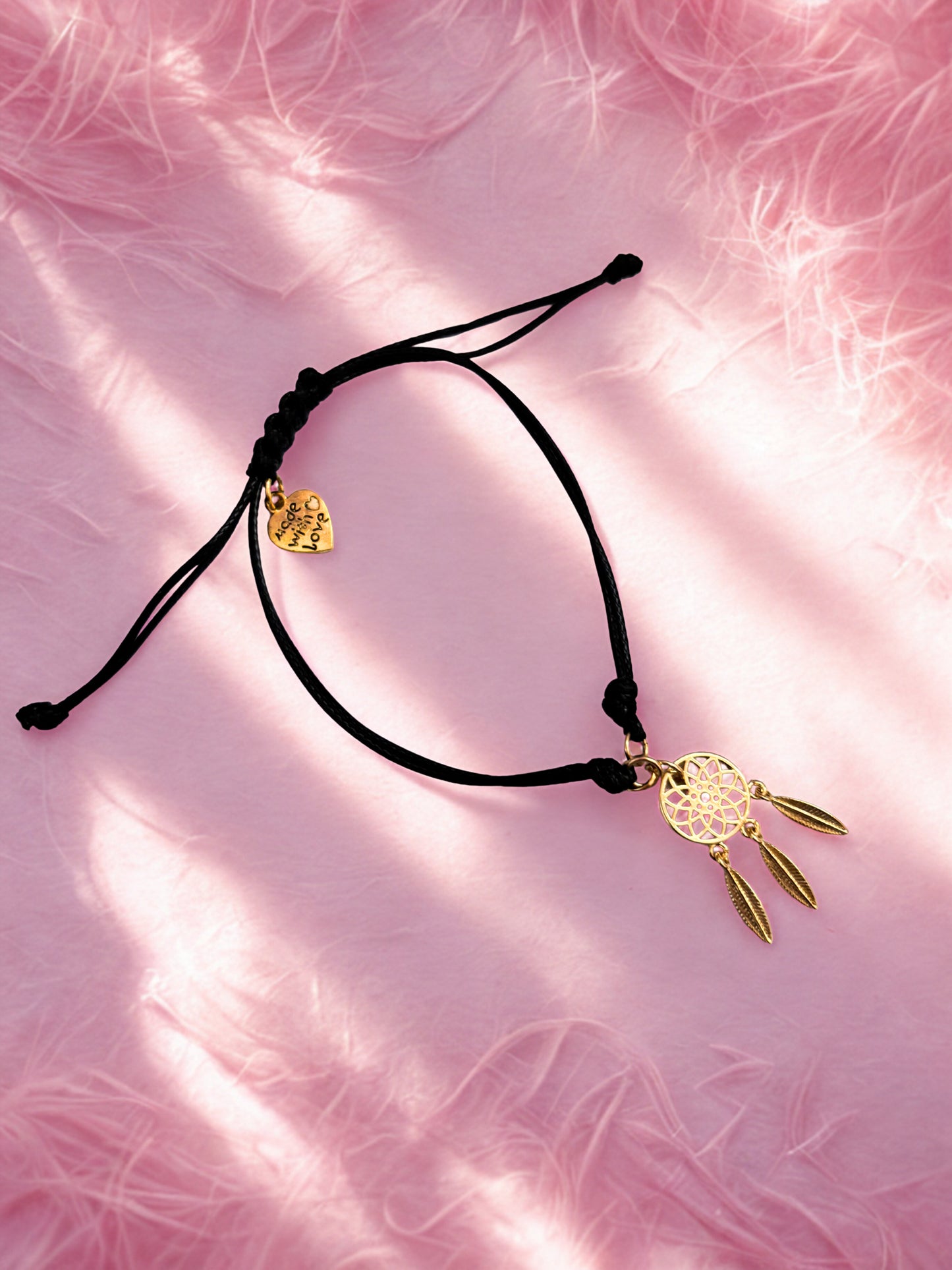 Black cord bracelet with gold dreamcatcher charm on a pink textured background