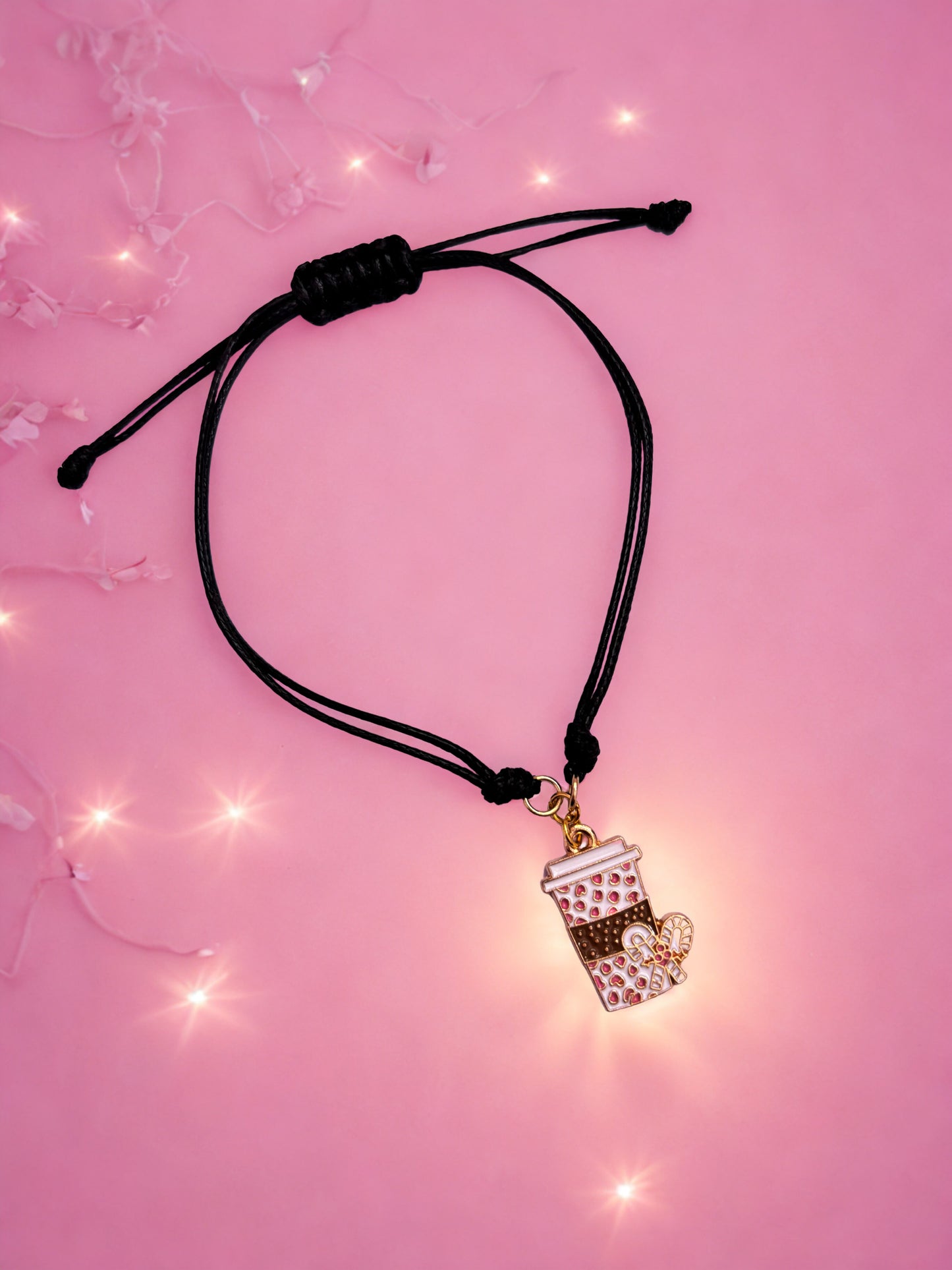 Bracelet with a coffee cup charm on a pink background with string lights