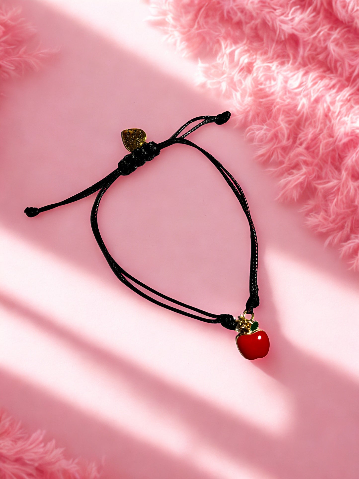 Black cord bracelet with apple charm on a pink background