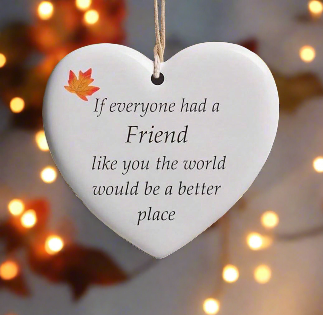 Heart-shaped ceramic plaque with a message and a leaf decoration, hanging against a blurred background with lights.