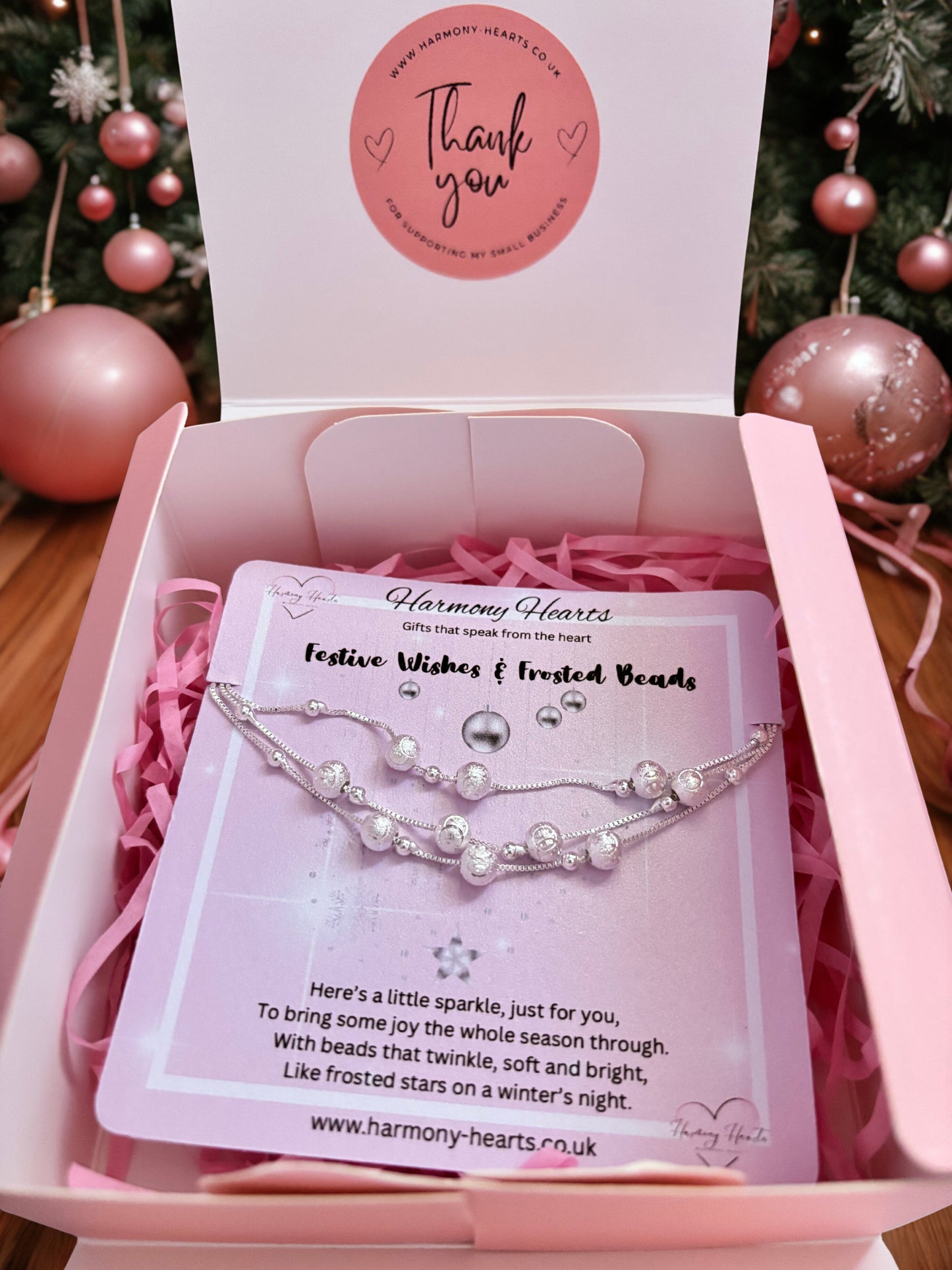 Bracelet in a pink box with 'Harmony Hearts' branding, surrounded by Christmas decorations.