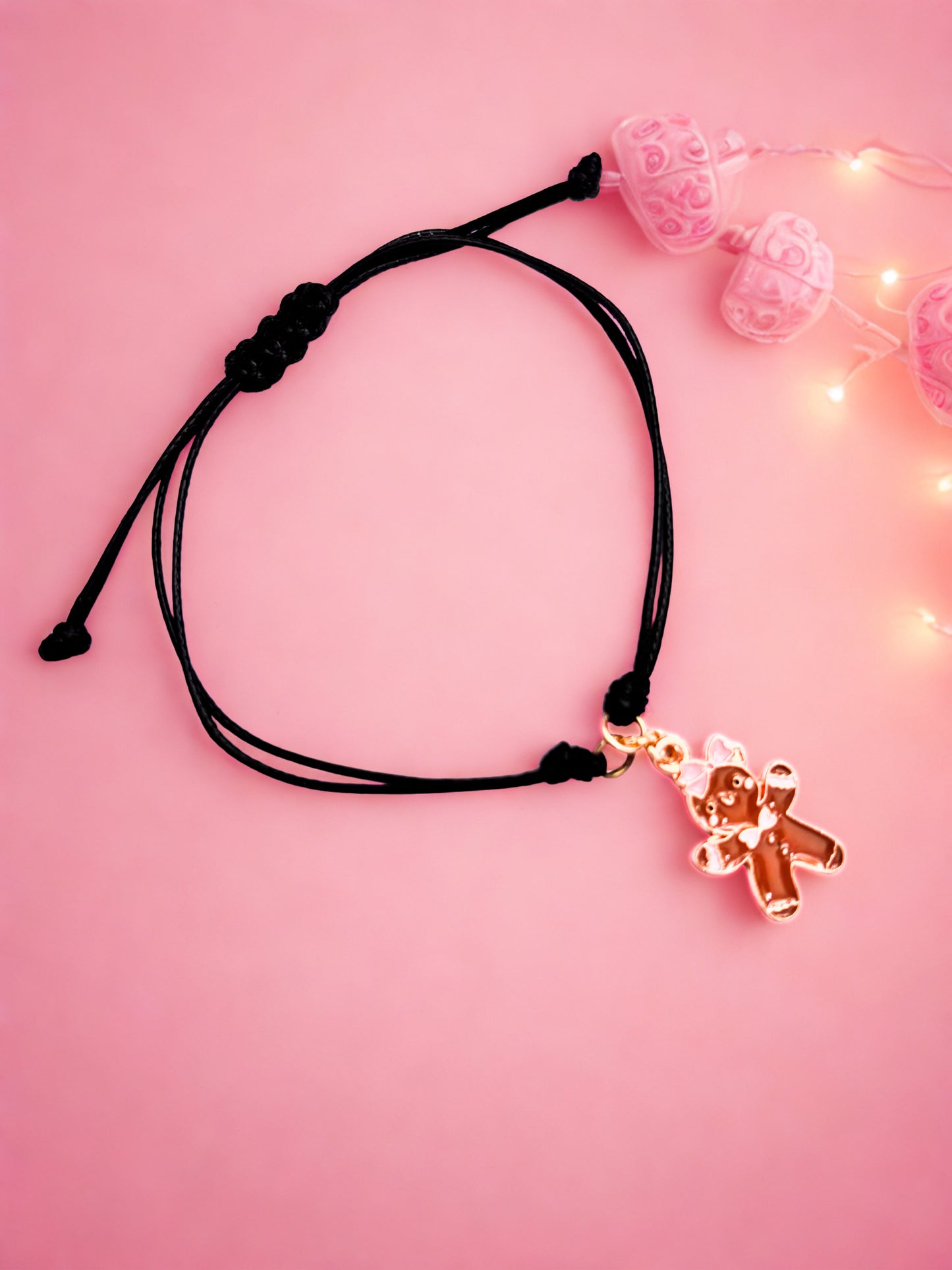 Black cord bracelet with gingerbread charm on a pink background