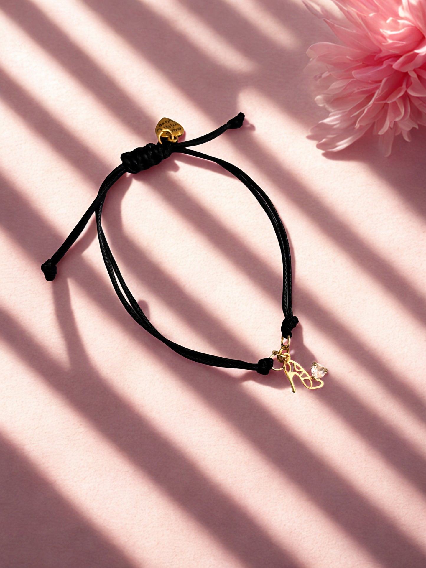 Black cord bracelet with gold shoe charm on a pink background