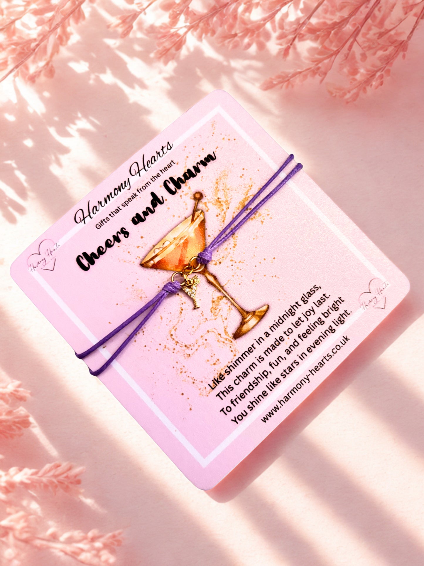 Pink poem card with a cocktail glass charm and purple cord bracelet on a pink background