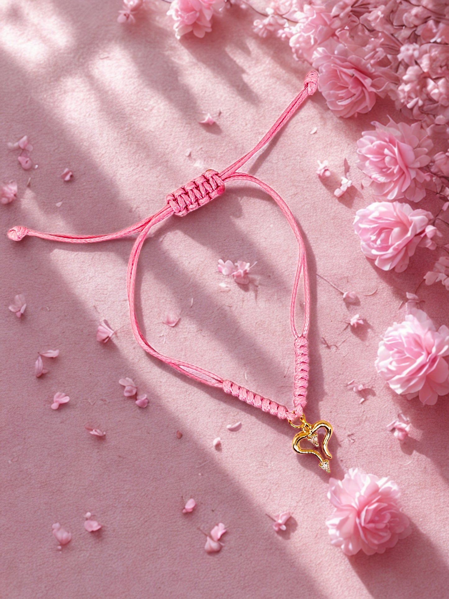 Pink bracelet with a gold heart charm on a pink floral background
