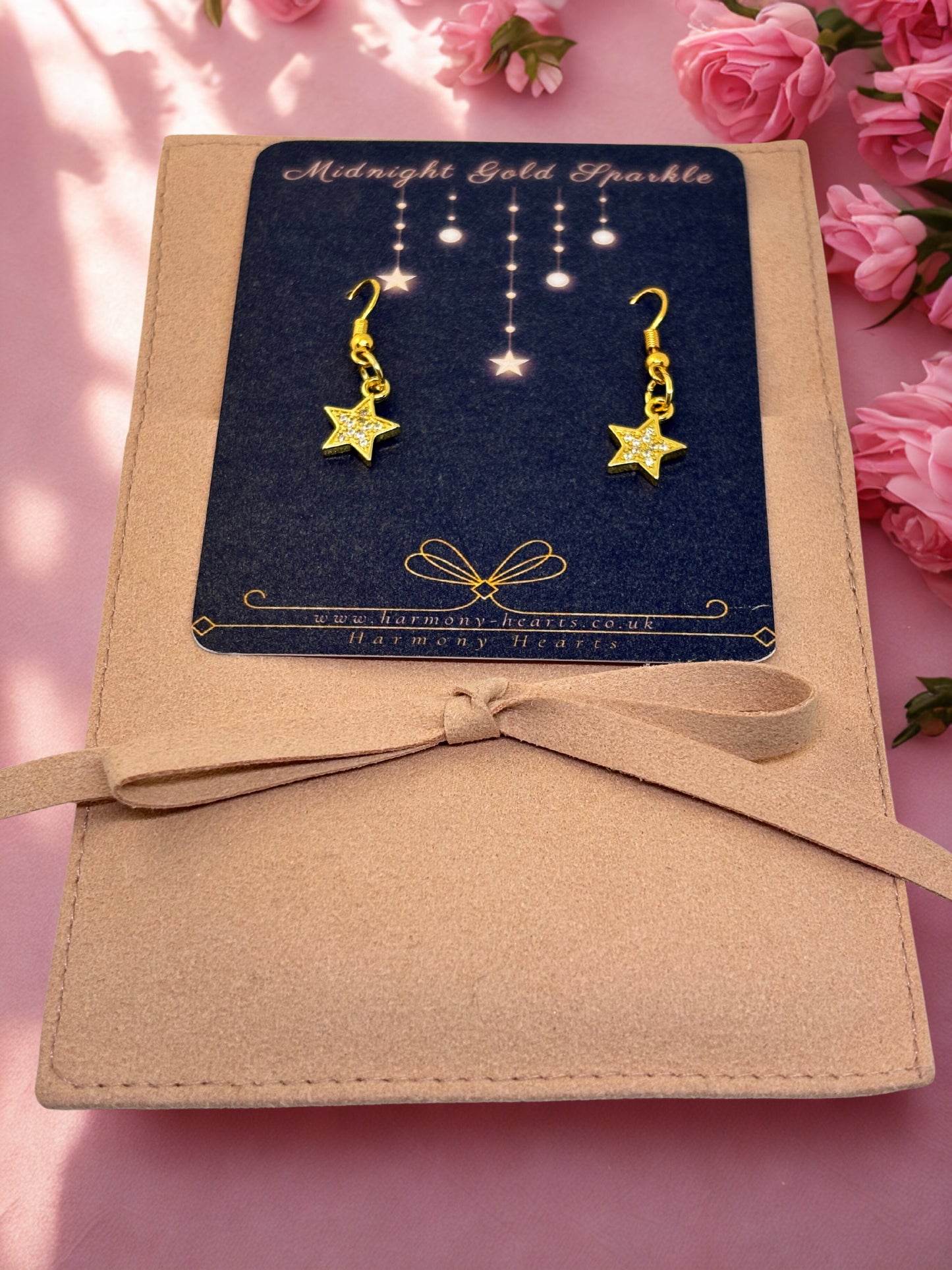 Gold star earrings on a branded card with pink flowers in the background