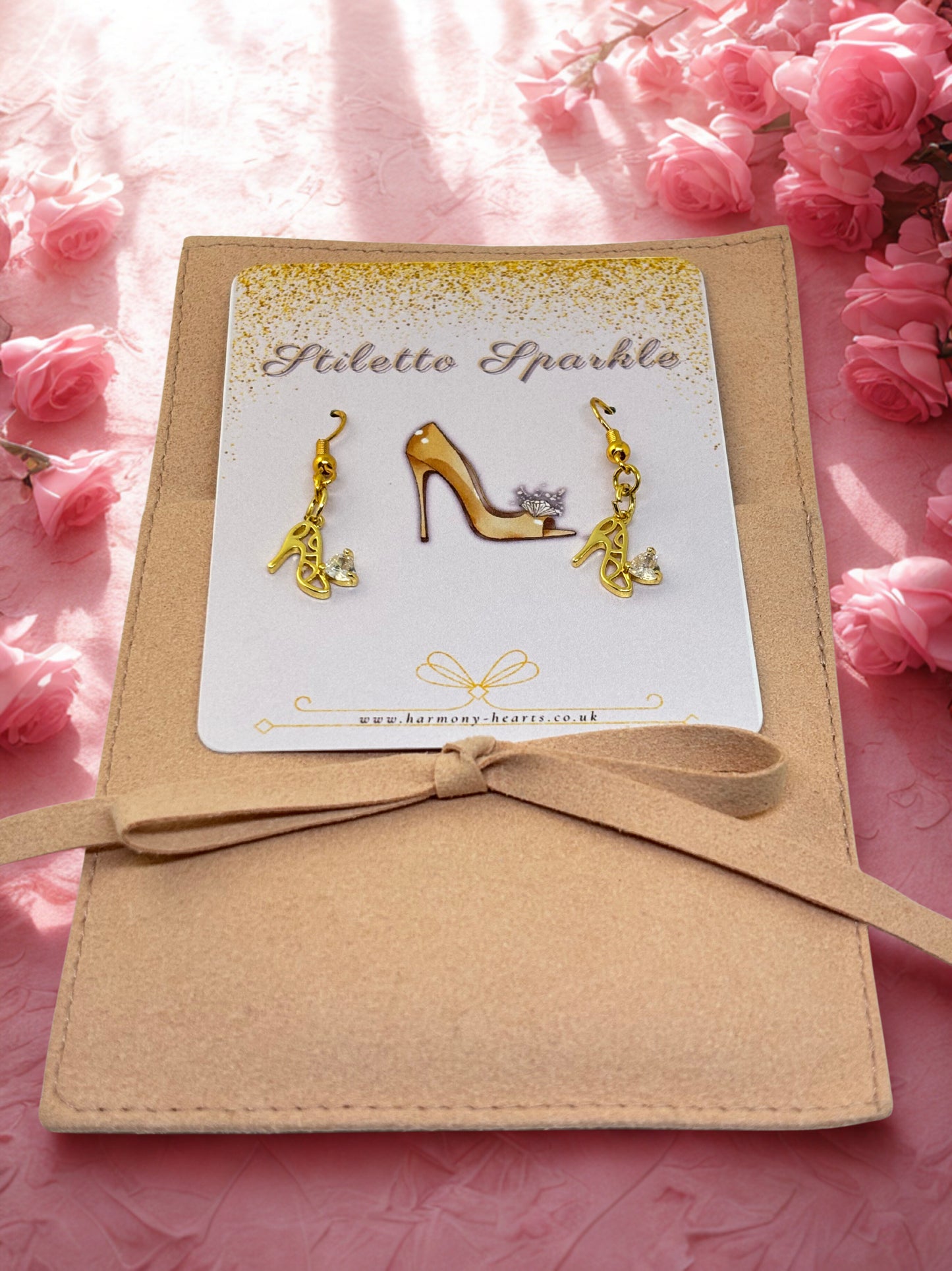 Gold high-heeled shoe earrings on a card with 'Stiletto Sparkle' branding, surrounded by pink flowers.