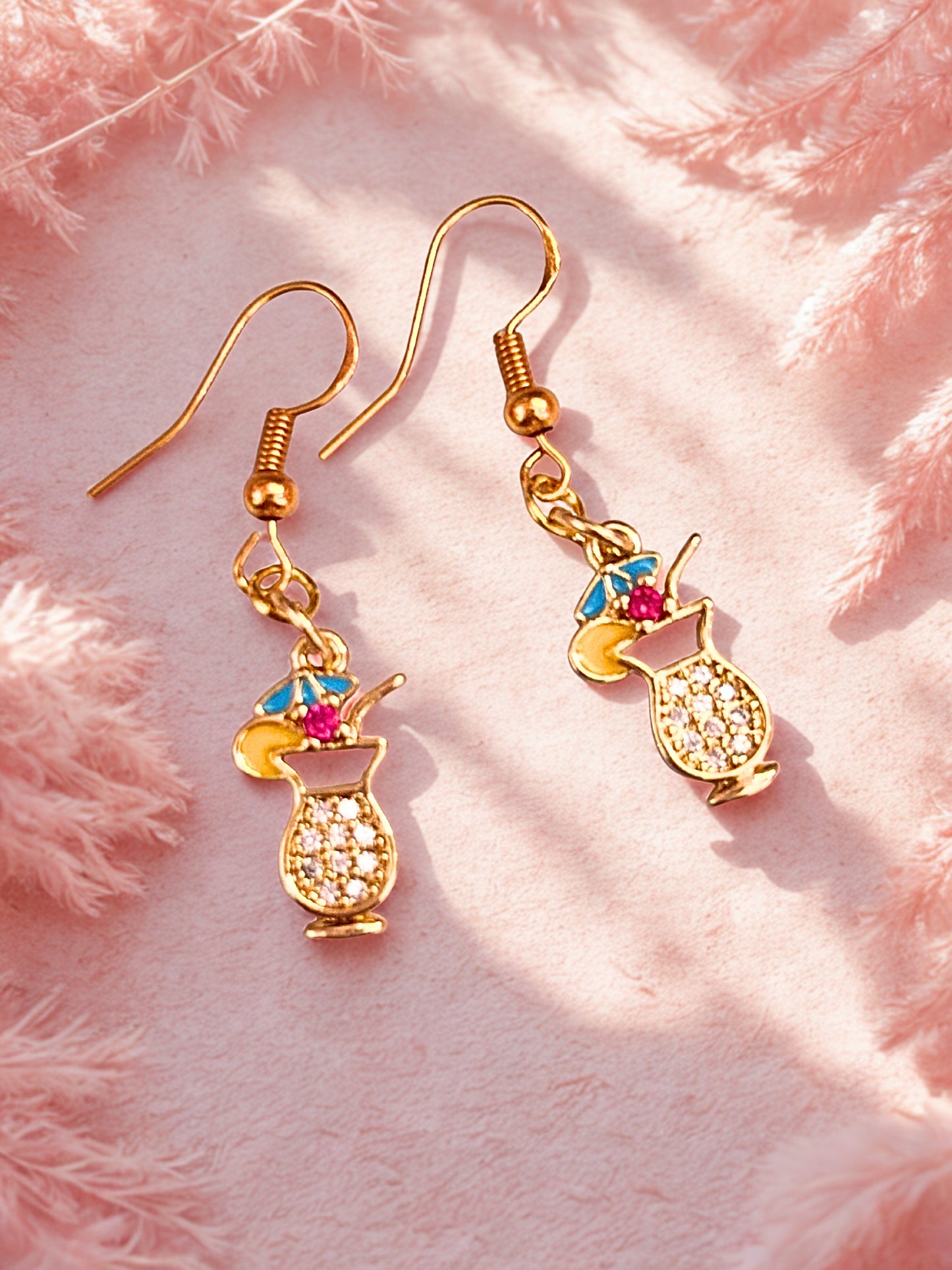 Gold cocktail glass earrings with colorful accents on a pink fluffy background