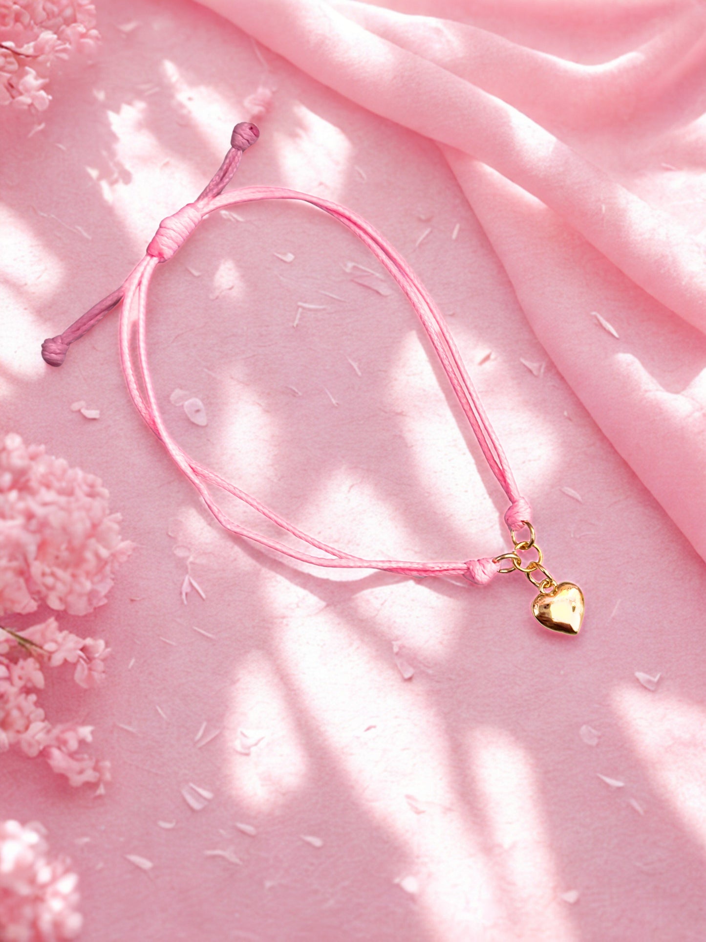 Pink bracelet with a gold heart charm on a pink fabric background